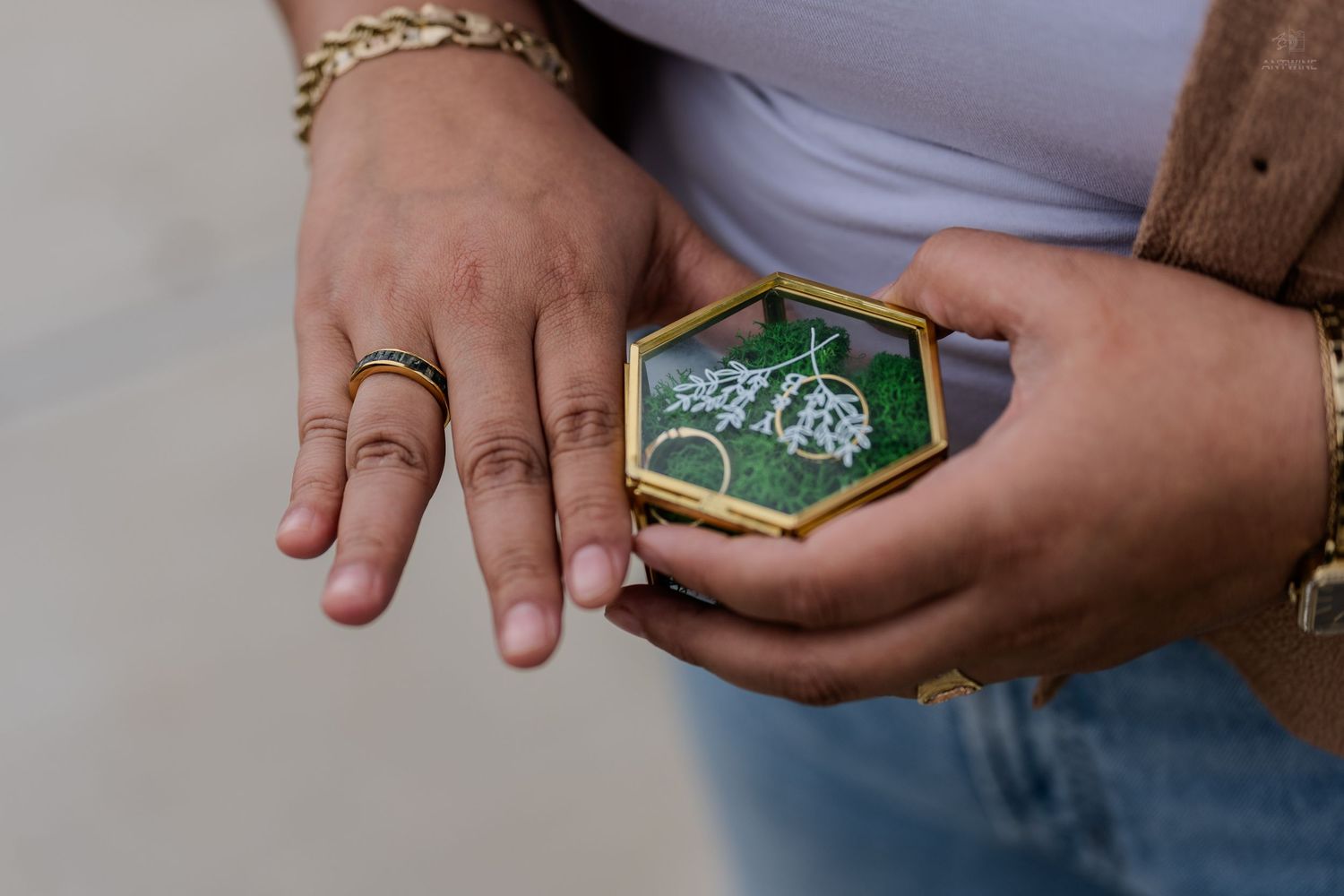 Hands wearing a gold ring holding open a hexagonal glass box with green moss interior.