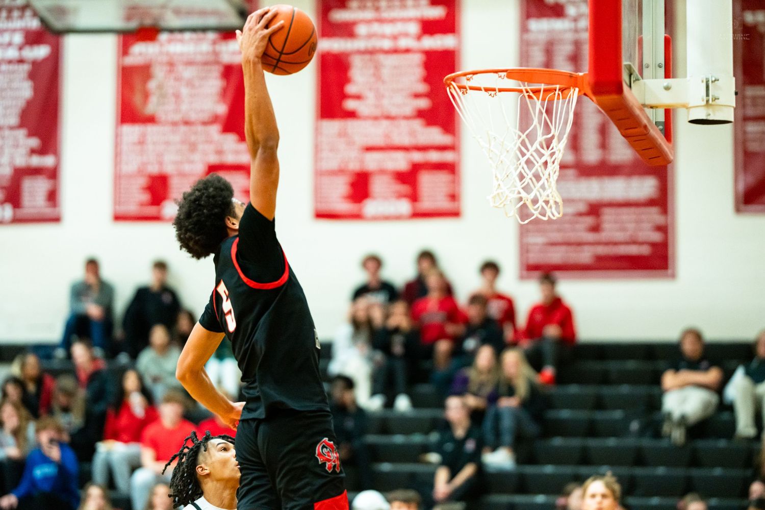 High school basketball player #5 executes impressive slam dunk over defender in gym.