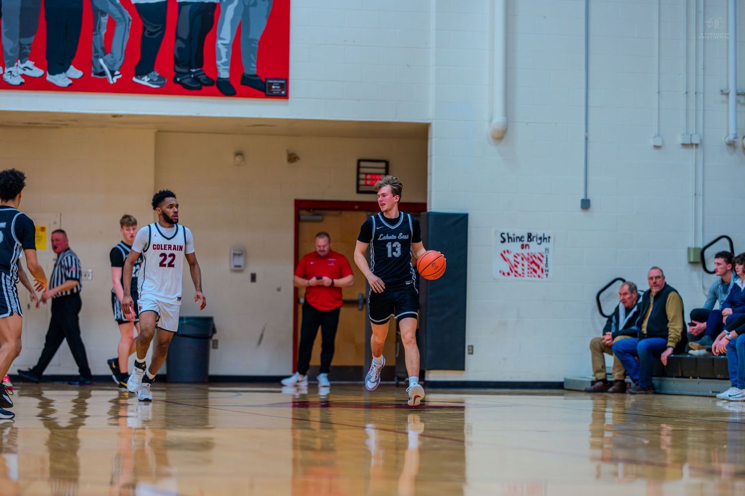 High school basketball player #13 in black uniform dribbles down the court during an indoor game.