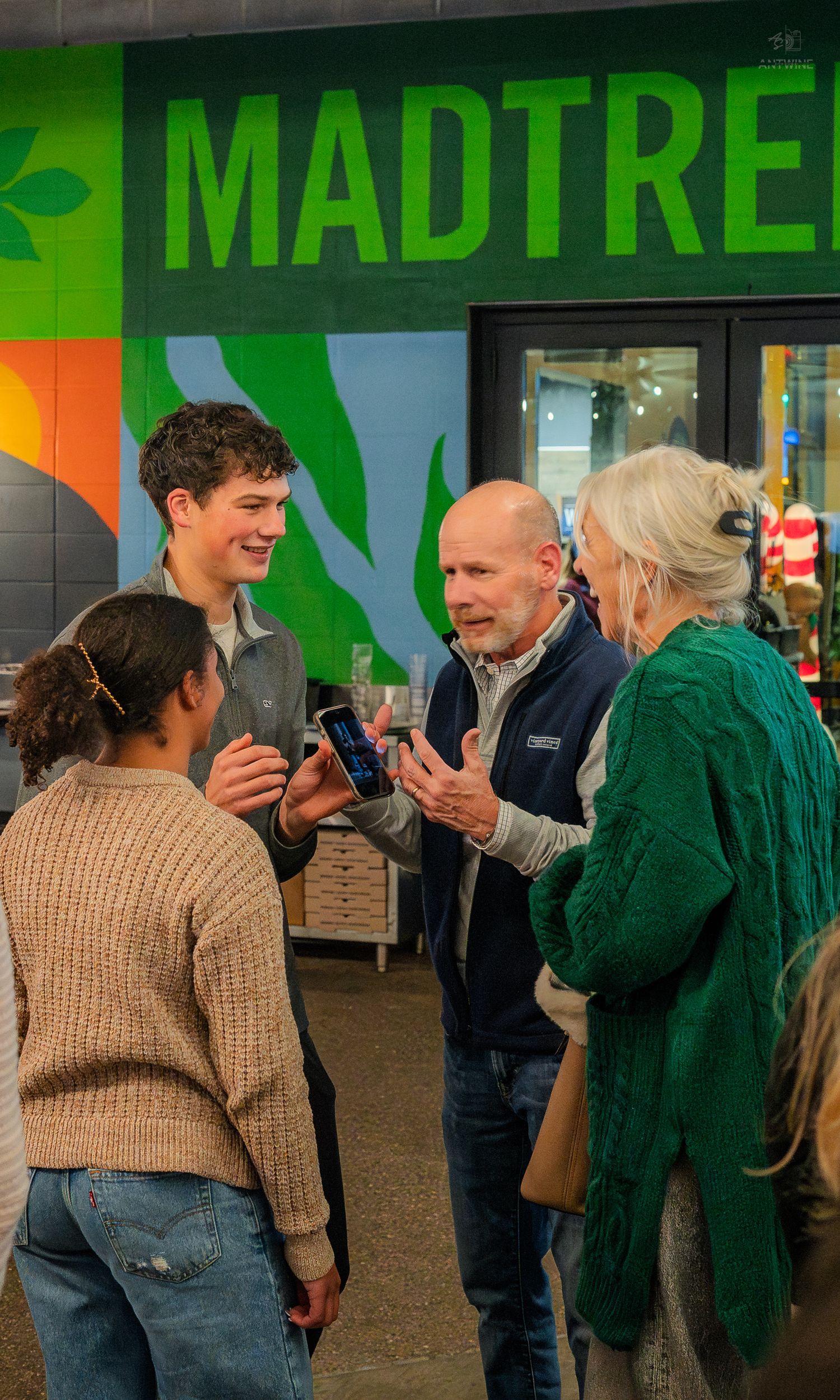 Group of people conversing and sharing phones outside MadTree Brewing entrance.