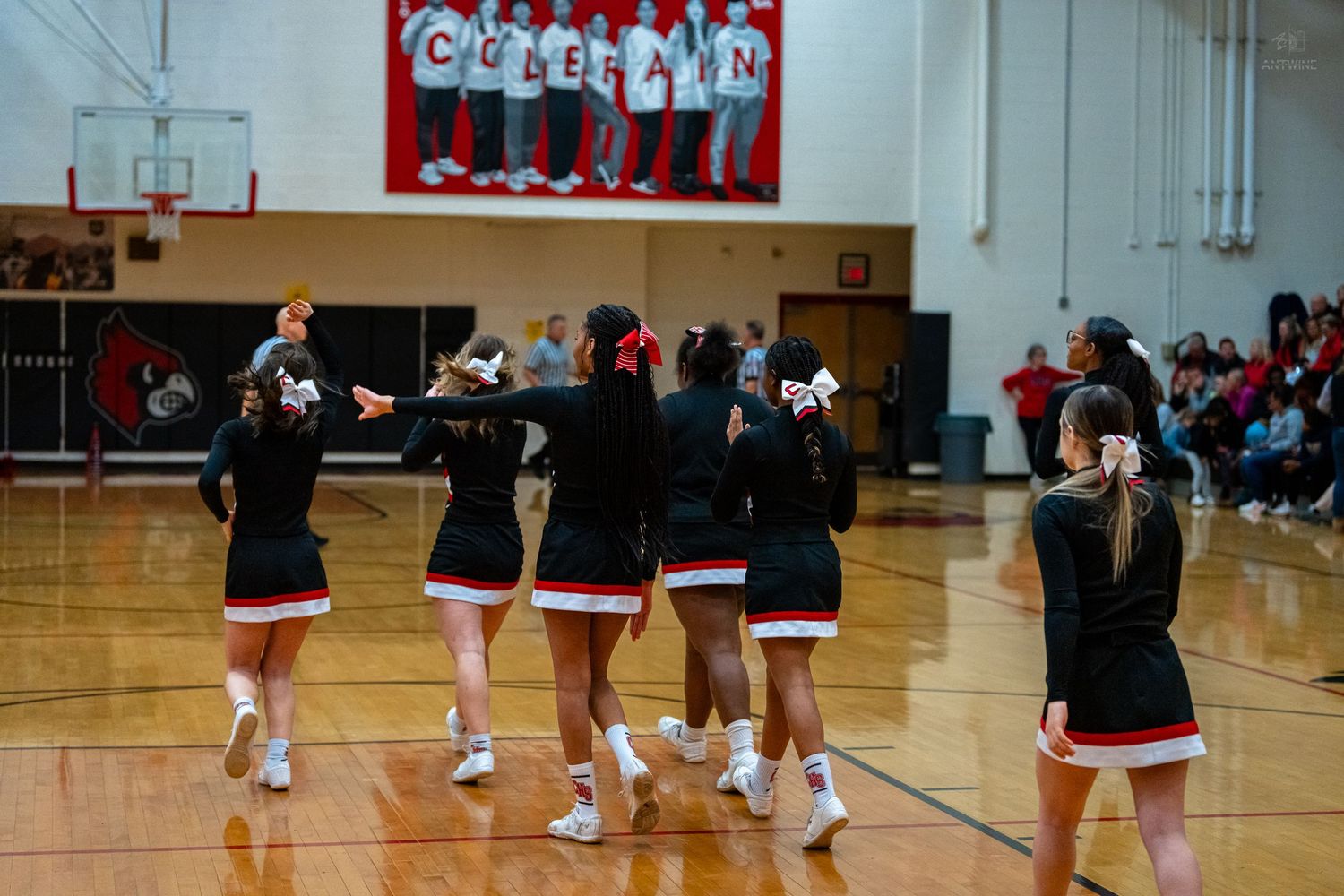 High school cheerleaders in black and red uniforms perform a routine on a basketball court.