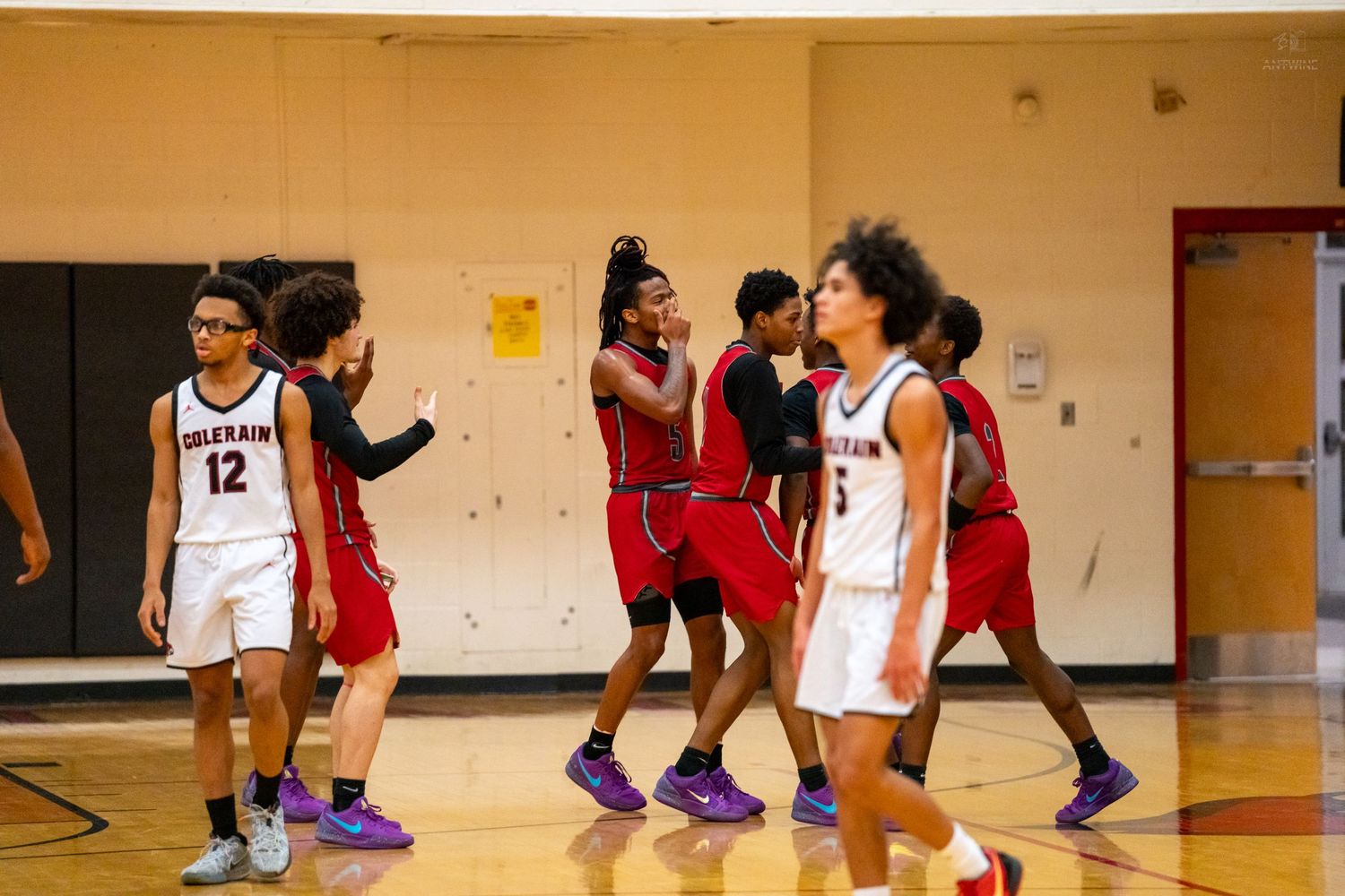 High school basketball players in red uniforms celebrate together on the court after a play.
