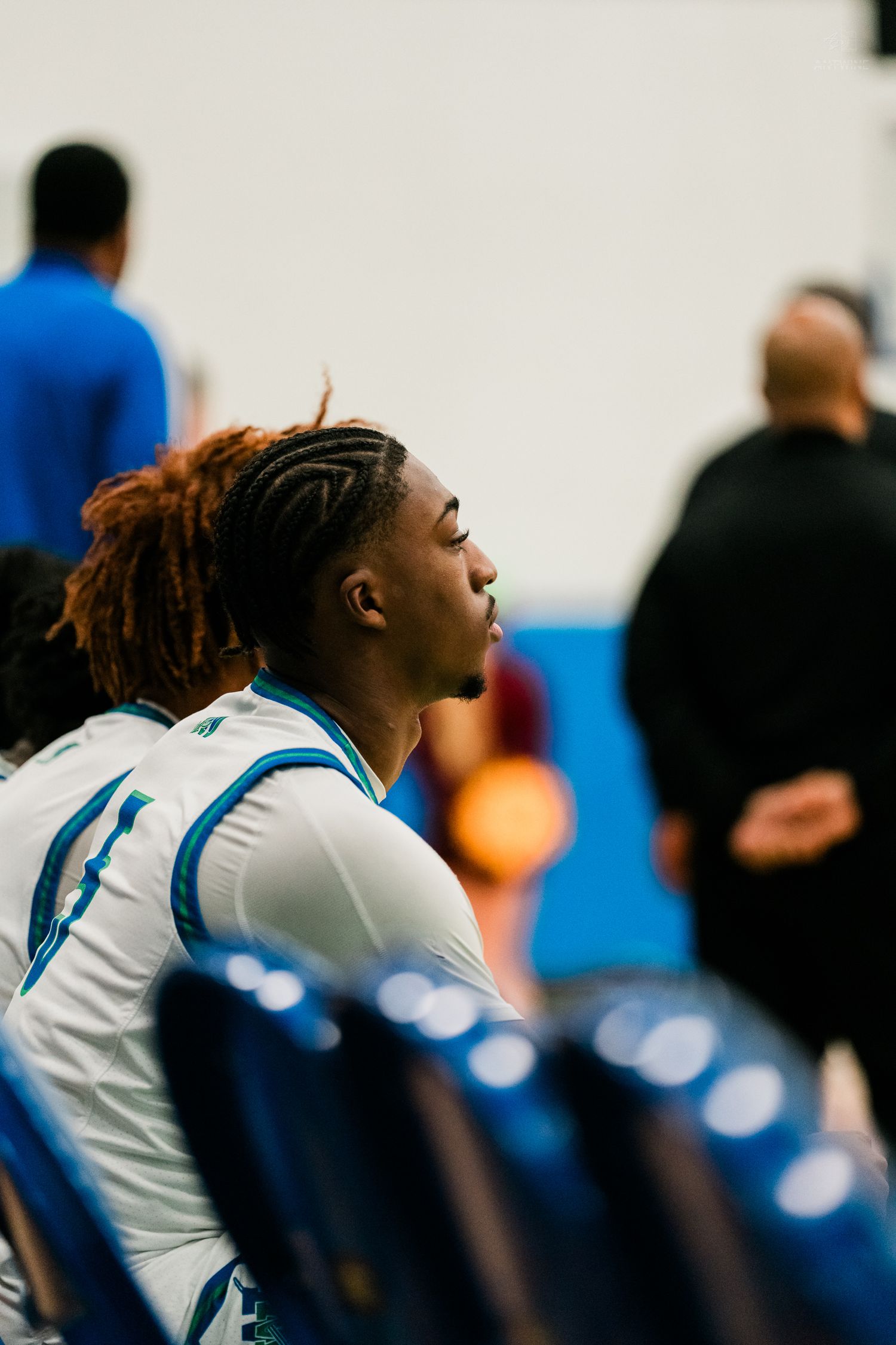 Young basketball player with braided hair sitting attentively on team bench.