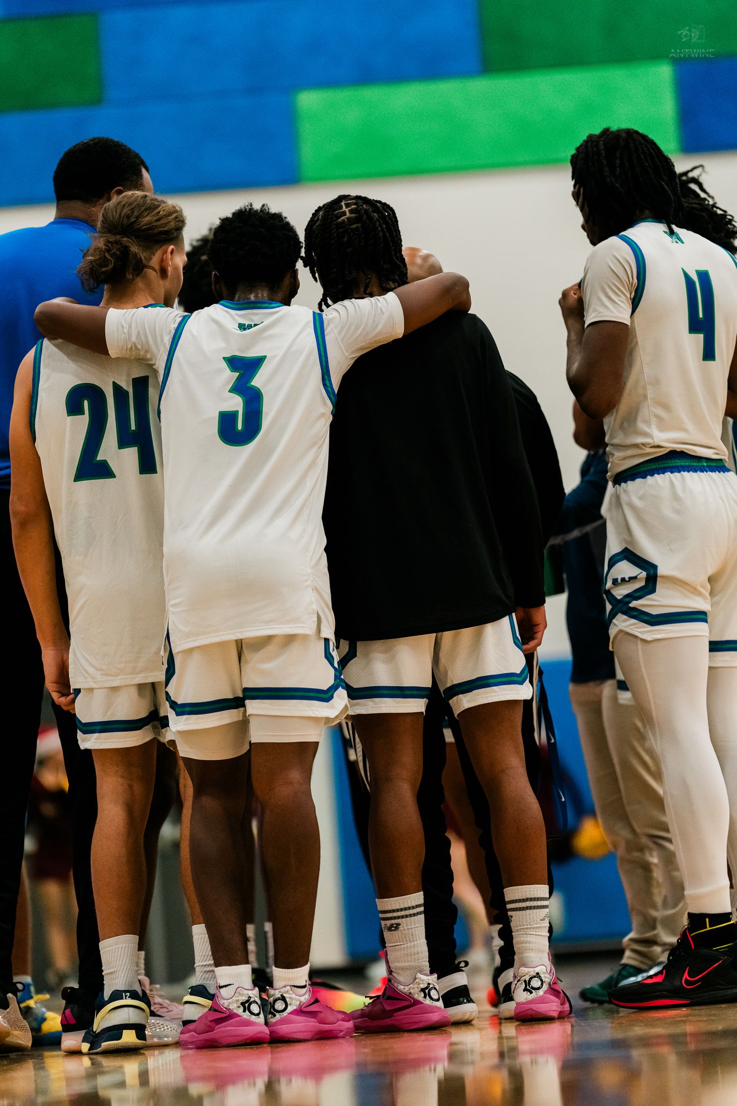 Warriors basketball players #24 and #3 huddle together on the sideline during a high school game.