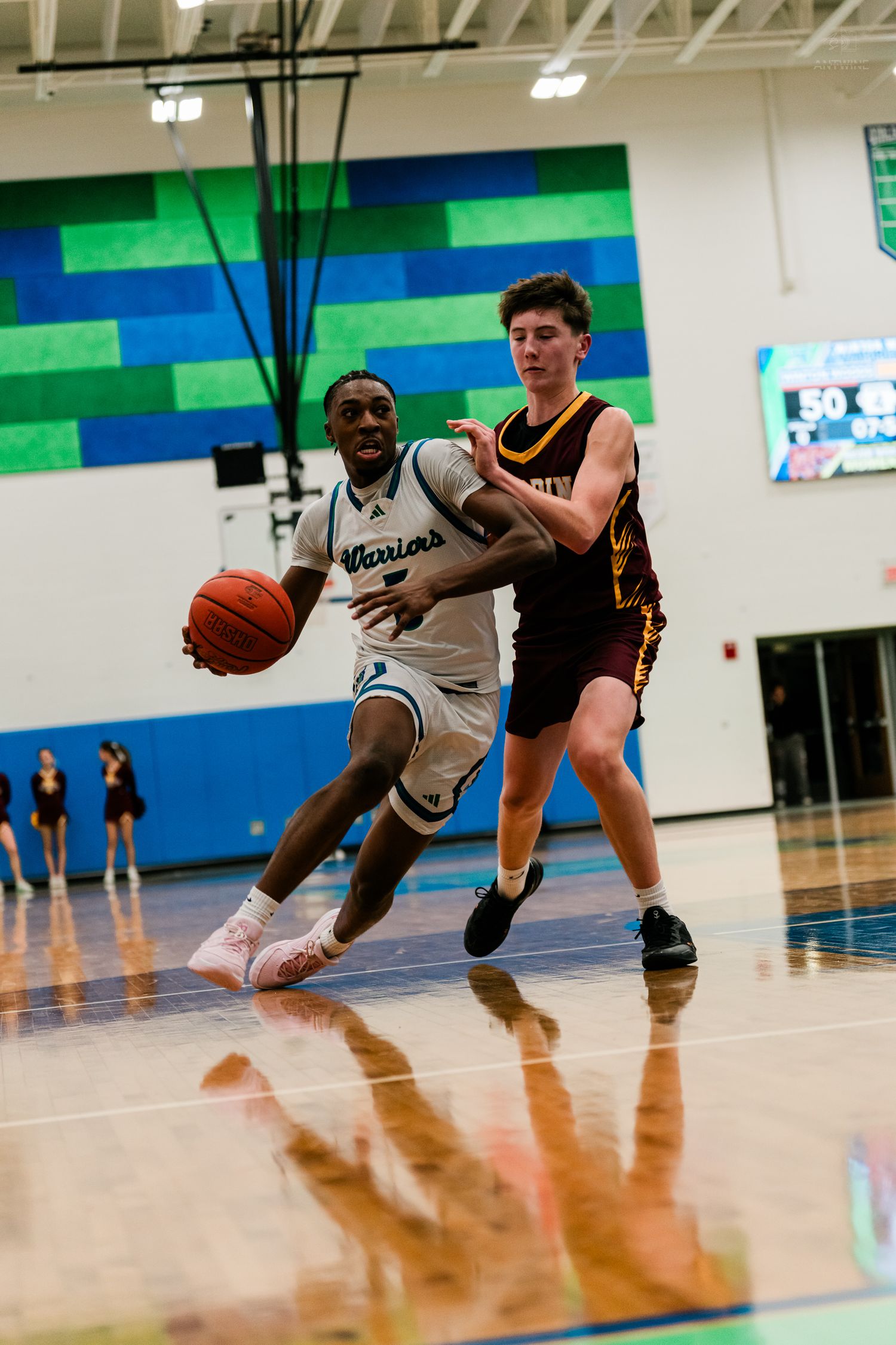 A Warriors player in white drives baseline past a tall maroon-uniformed defender during a basketball game.