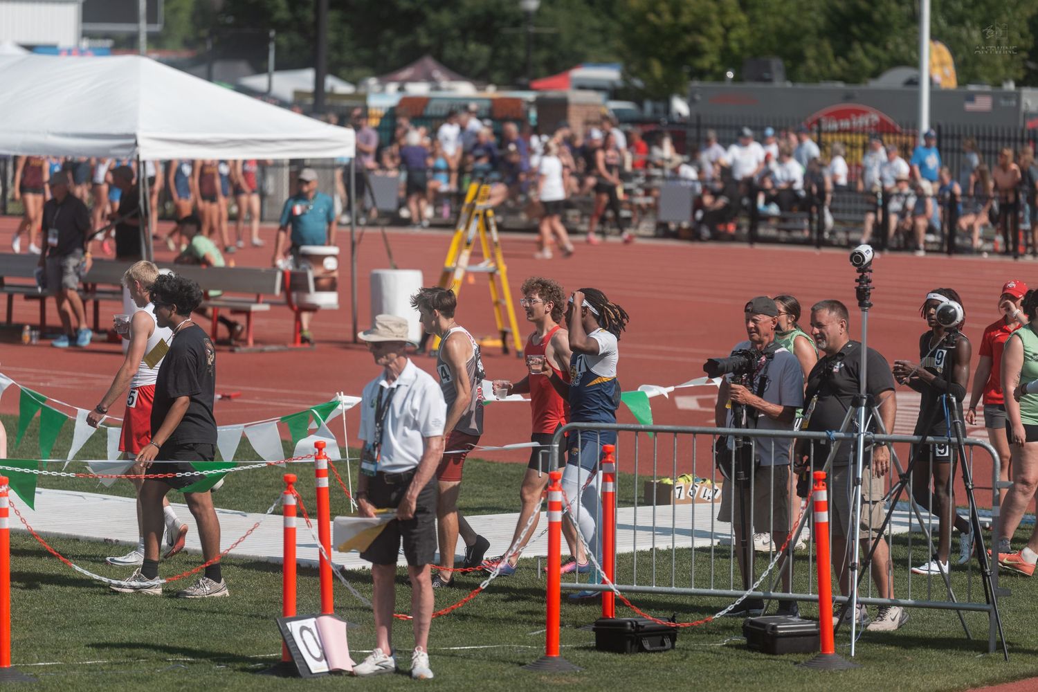 Track and field officials and athletes gather near a finish line barrier at an outdoor athletic competition.