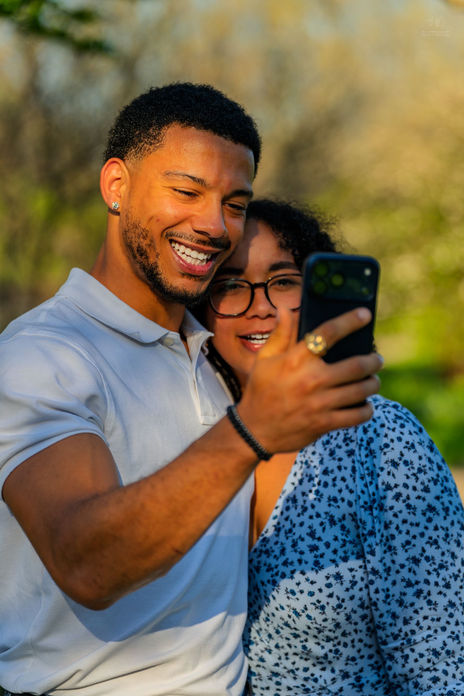Joyful couple taking a selfie together outdoors in golden sunlight, both smiling at the phone screen.