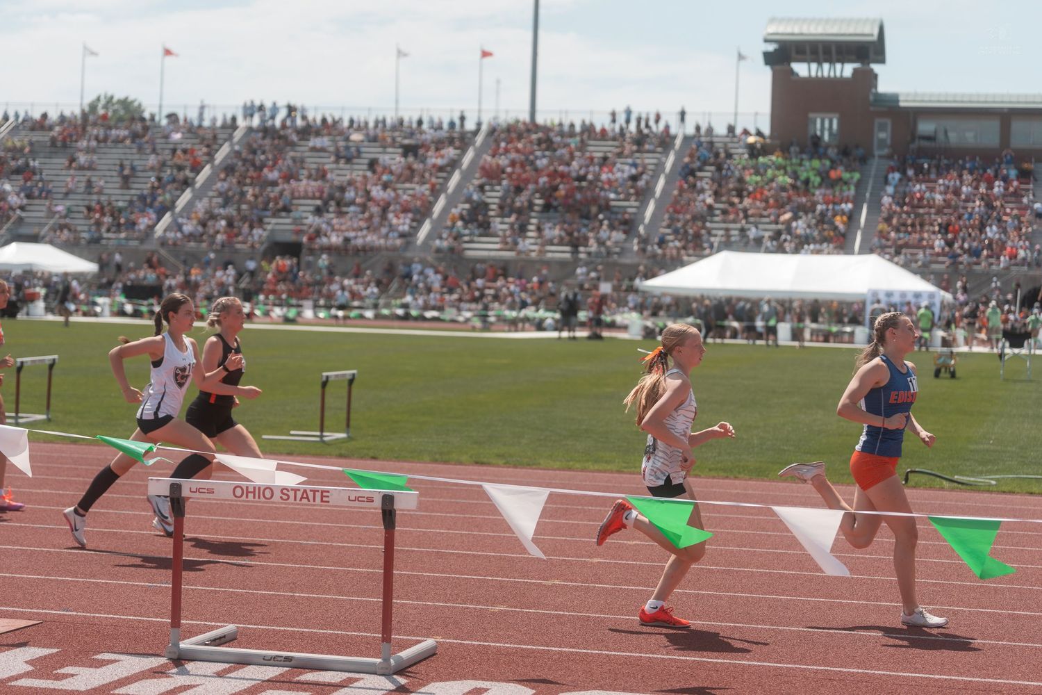 Female runners race past hurdles at the Ohio State University outdoor track and field championship.