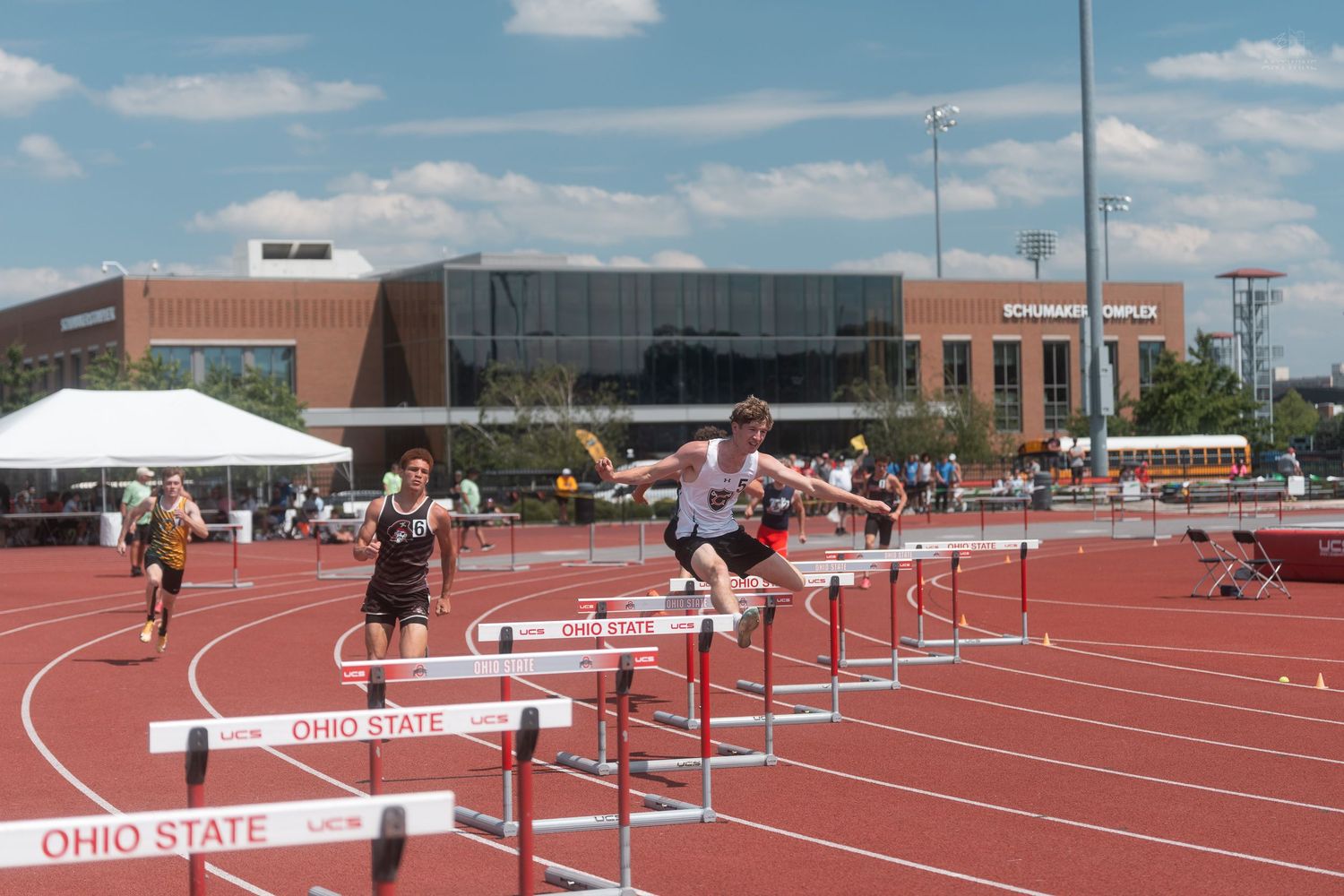 Athletes leap over hurdles on the Ohio State University track during an OHSAA championship meet on a sunny day.