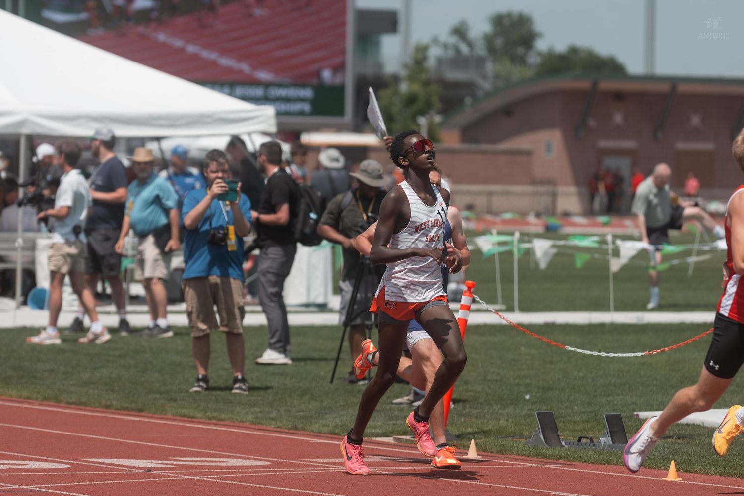 African American male athlete runs on a red track during an outdoor track and field championship competition.