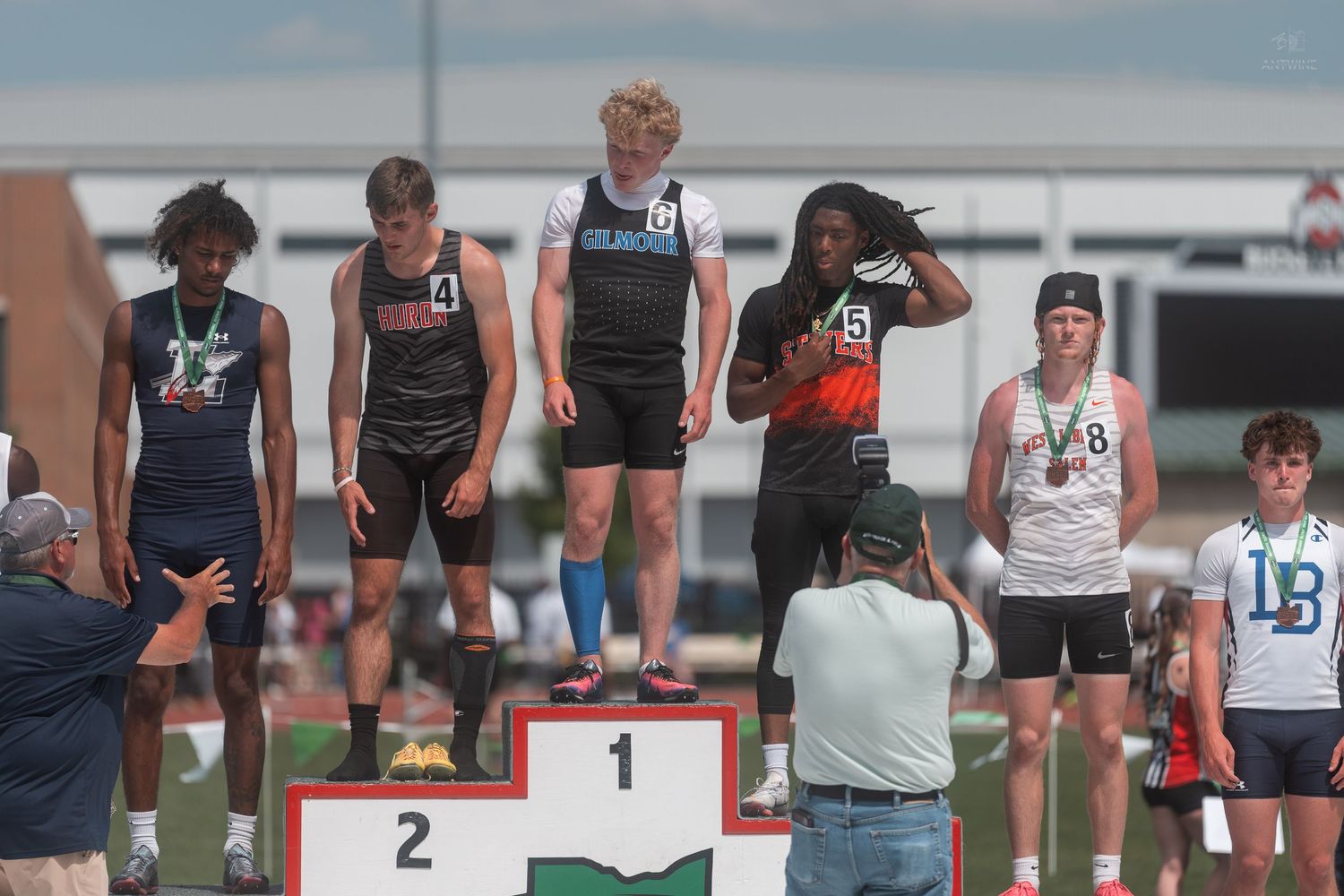 Teen male athletes celebrate on numbered award podium at OHSAA outdoor track and field championship.