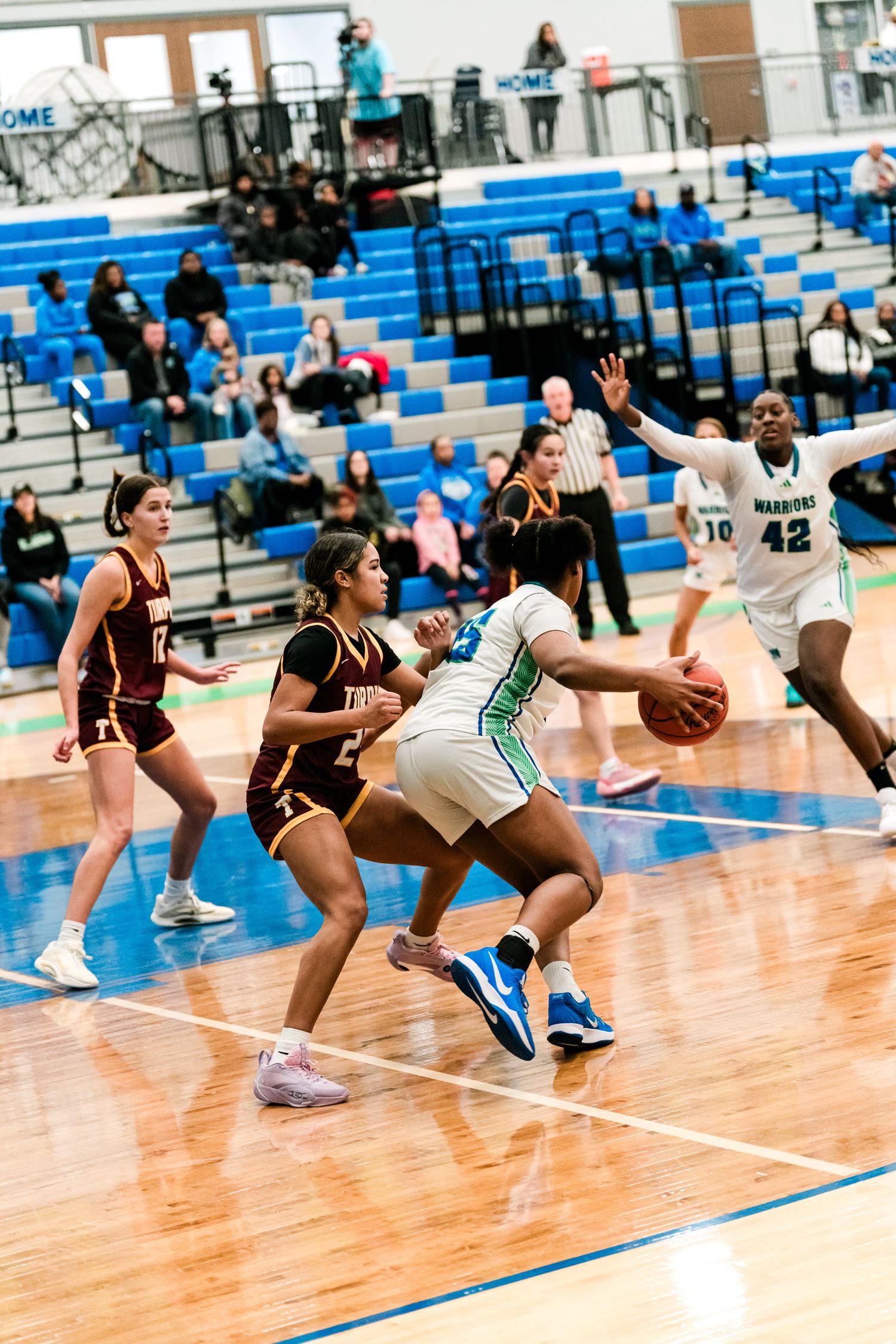 Girls high school basketball players battle near the basket as a defender in white drives toward the hoop against maroon team.