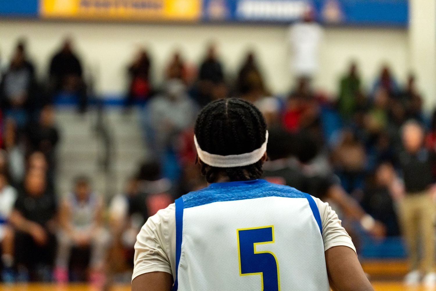 Basketball player #5 in white and blue jersey stands at the free throw line with crowd in background.