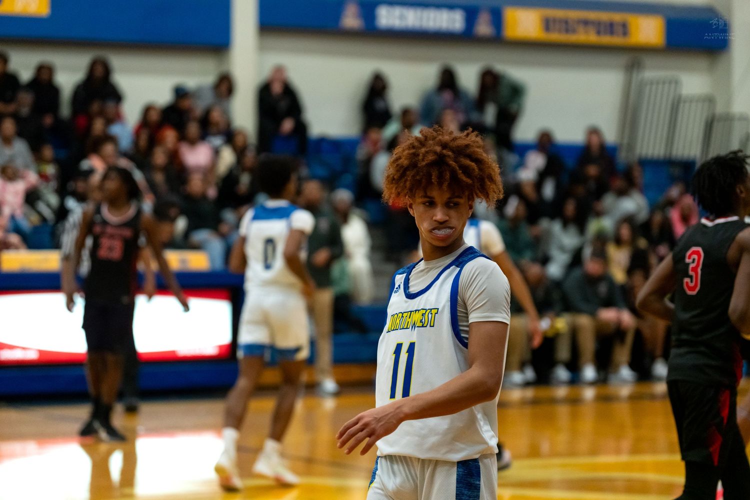 A high school basketball player wearing number 11 stands on the court during a game.