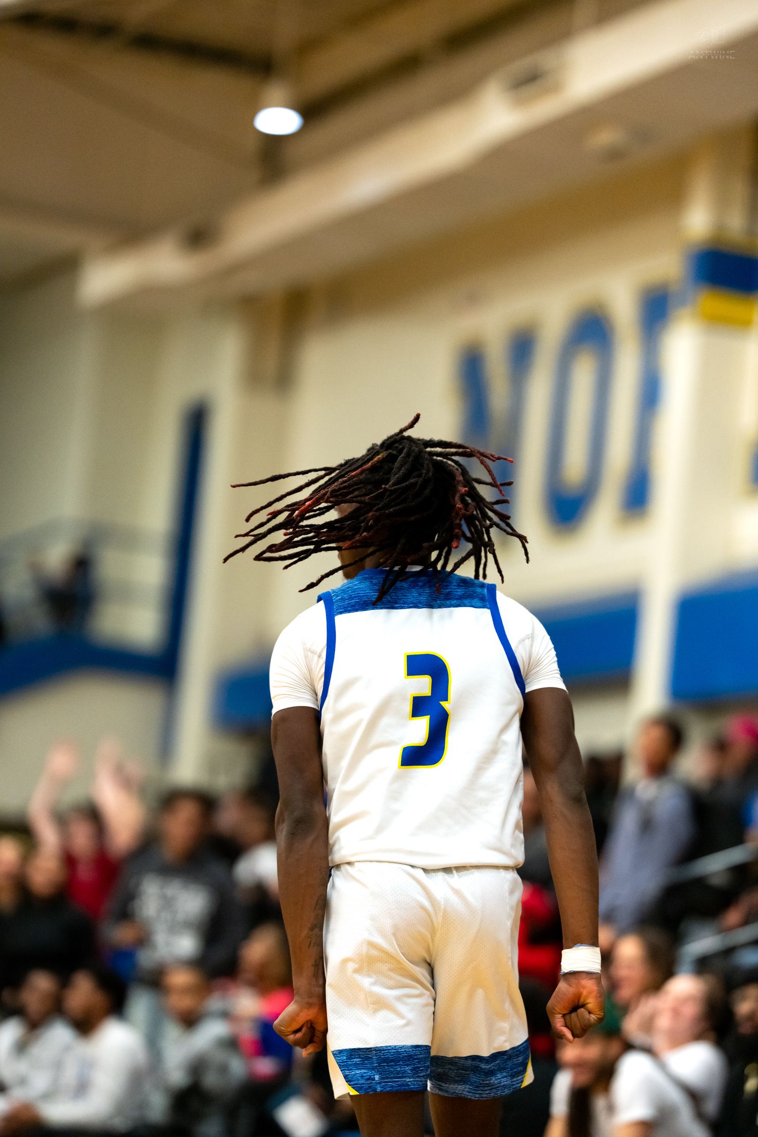High school basketball player number 3 with dreadlocks celebrates in front of a home crowd.