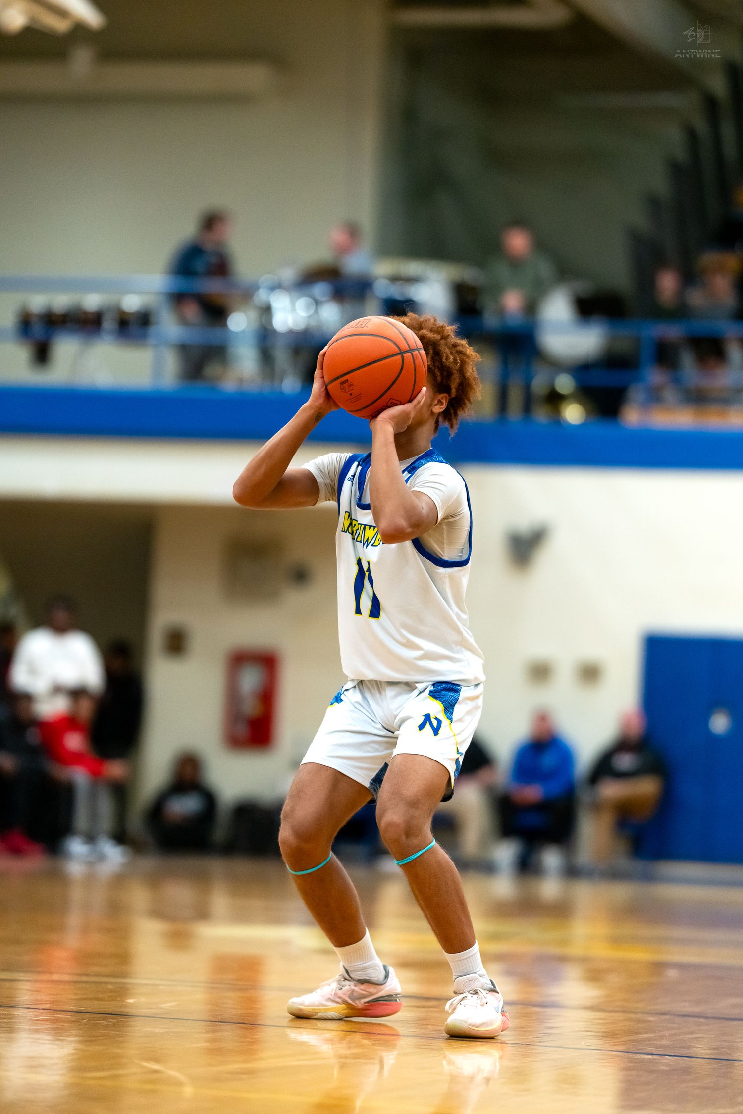 Northwest high school basketball player #11 raises ball to shoot during an indoor basketball game.