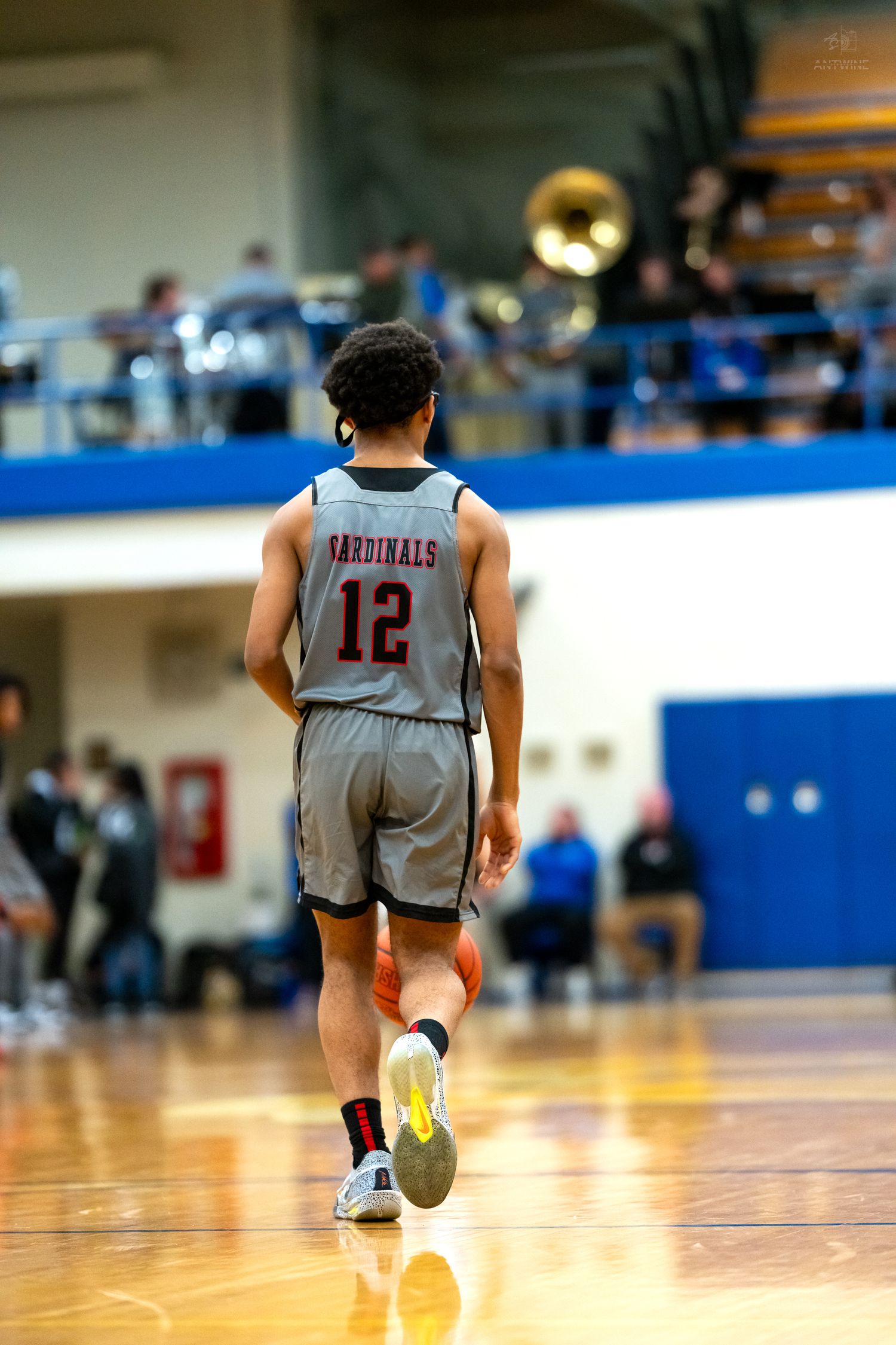Cardinals player #12 in gray jersey walks on hardwood court during high school basketball game.