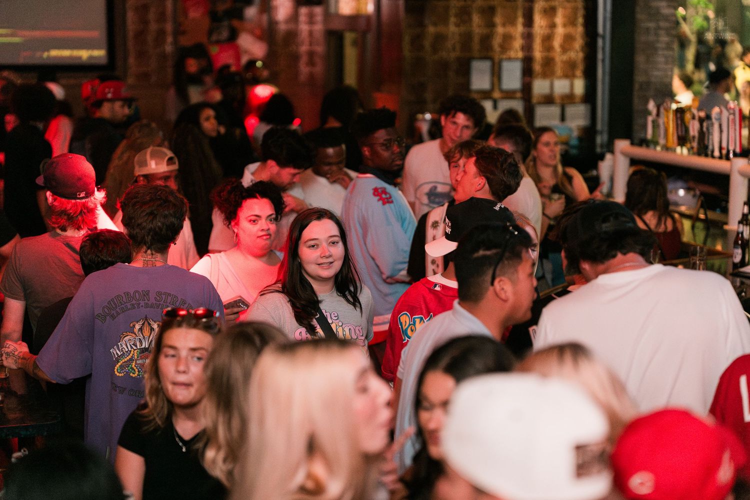 Packed bar scene with diverse group of young adults socializing under red ambient lighting.