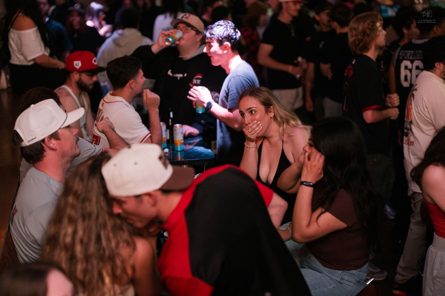 Group of young people laugh and socialize while seated at a lively nightclub or bar event.