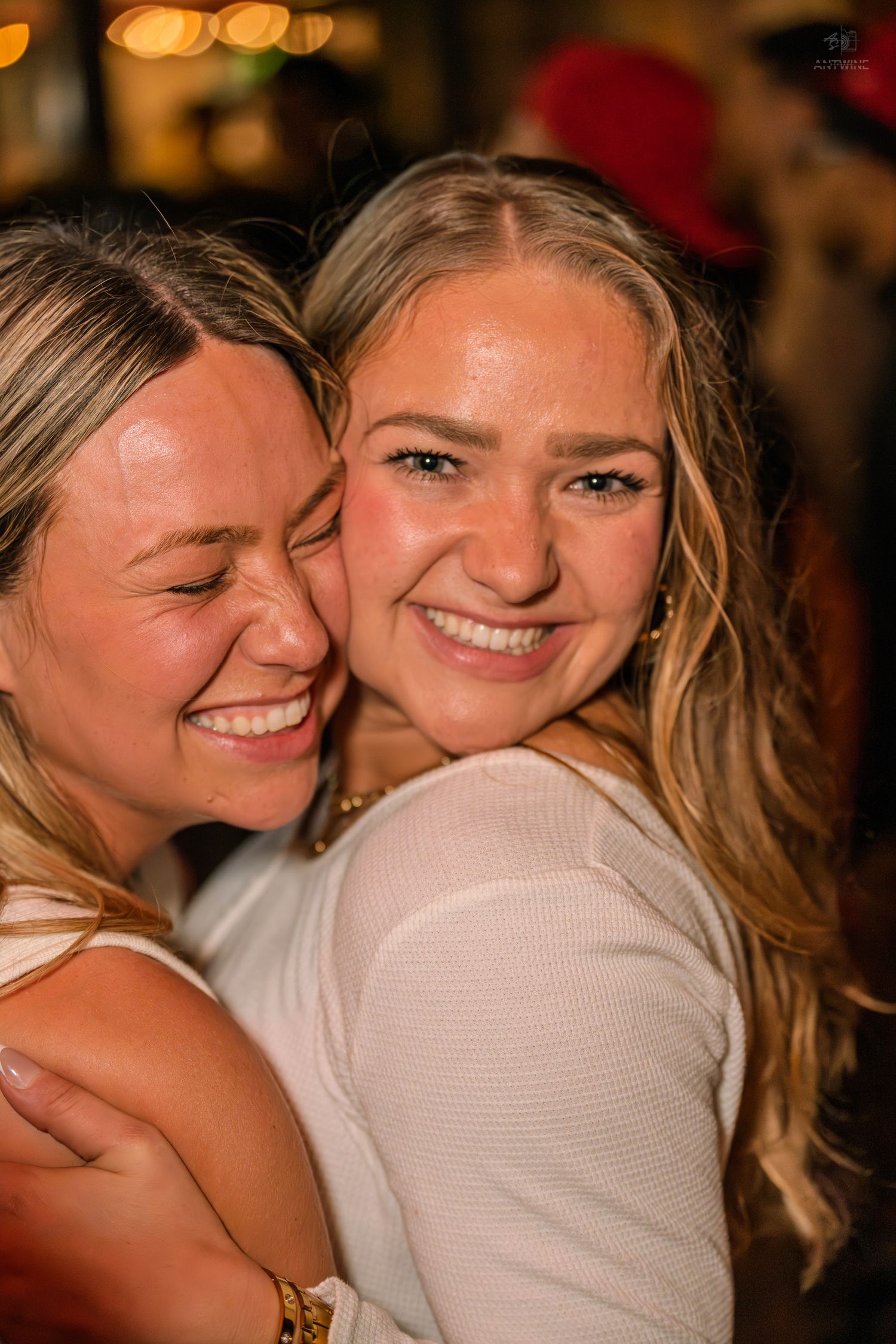 Two happy young women hug and smile warmly at a lively nightclub gathering.