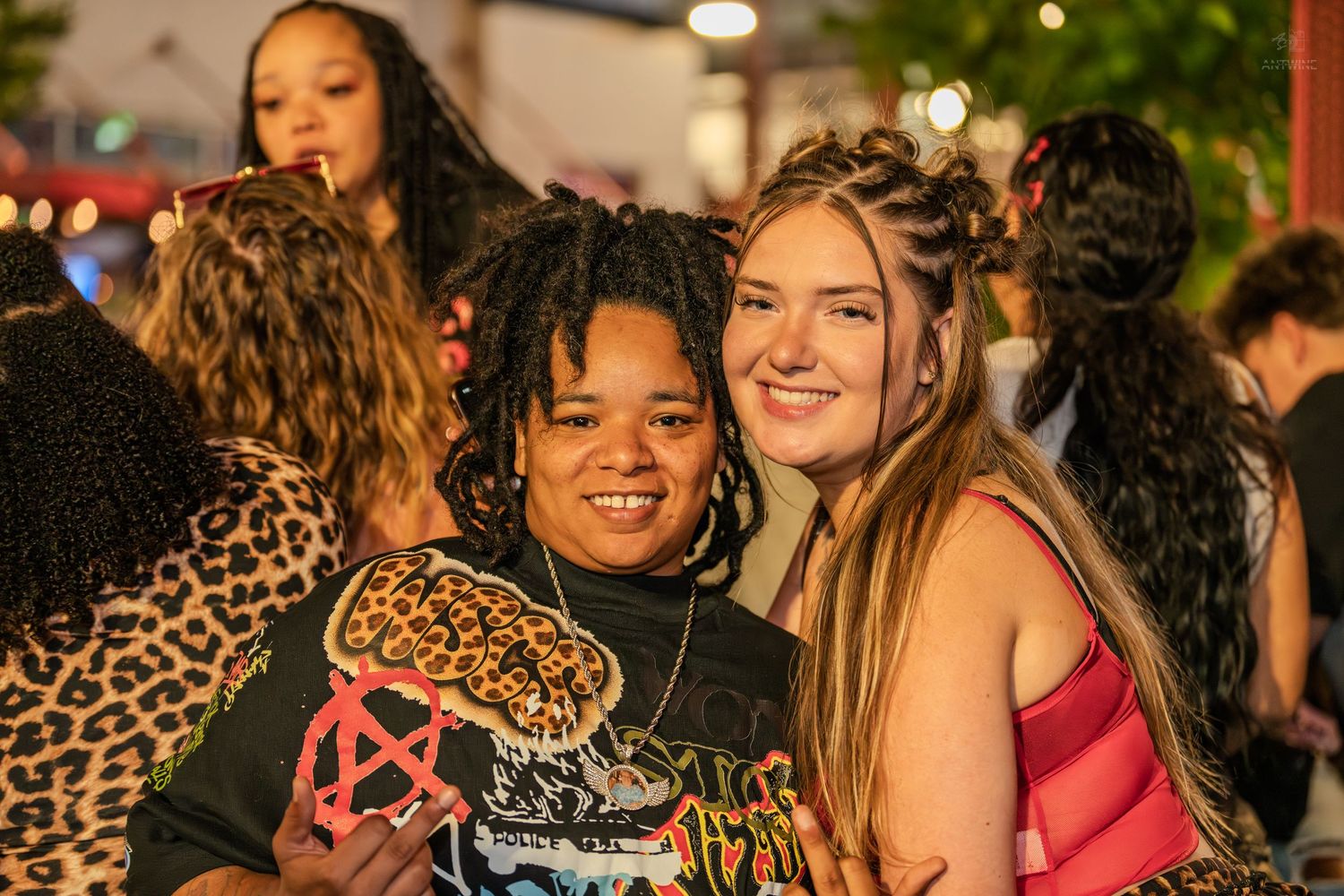 Two smiling young friends posing together at an outdoor nighttime social event.