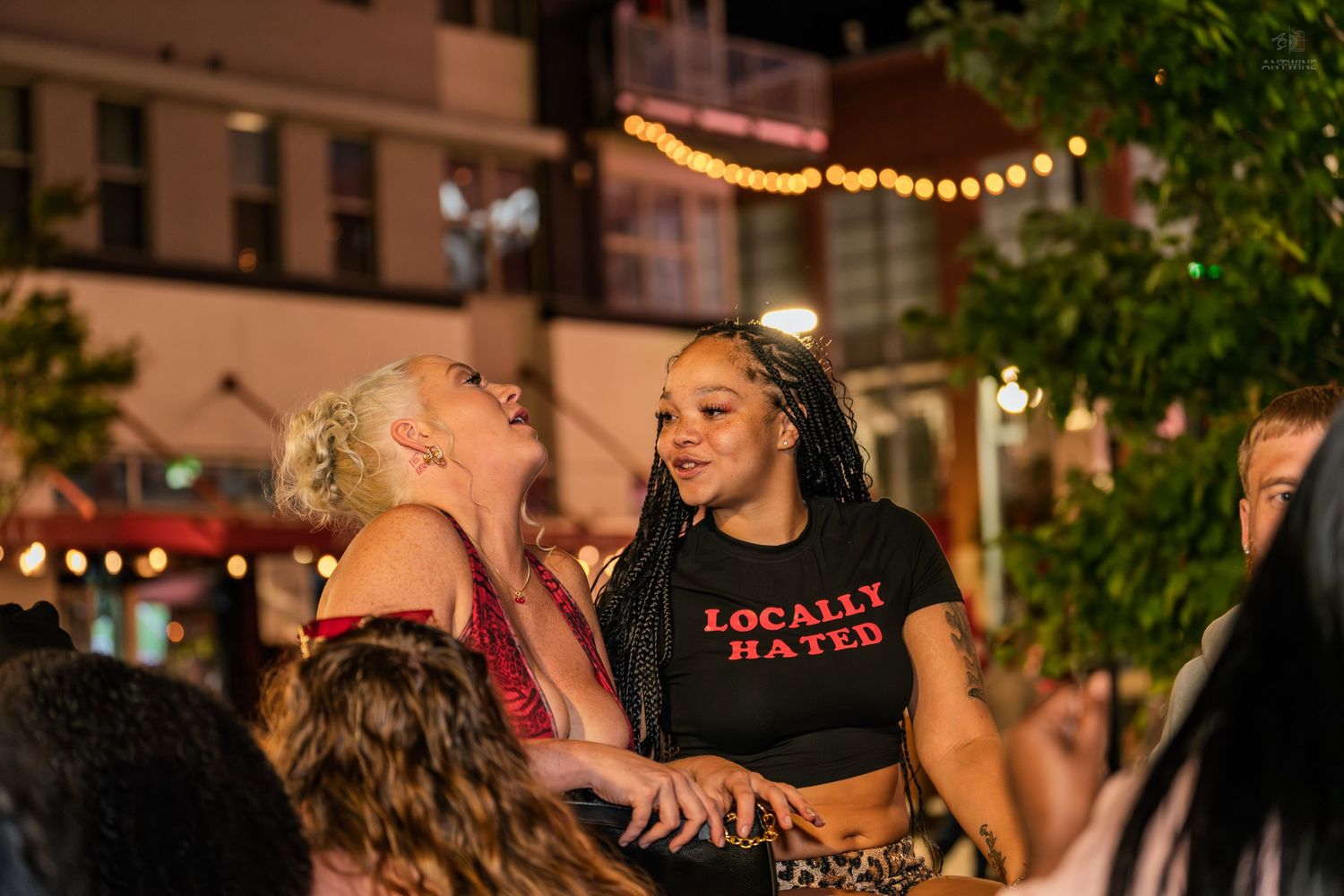 Two women dancing and socializing at an outdoor nighttime event with string lights.