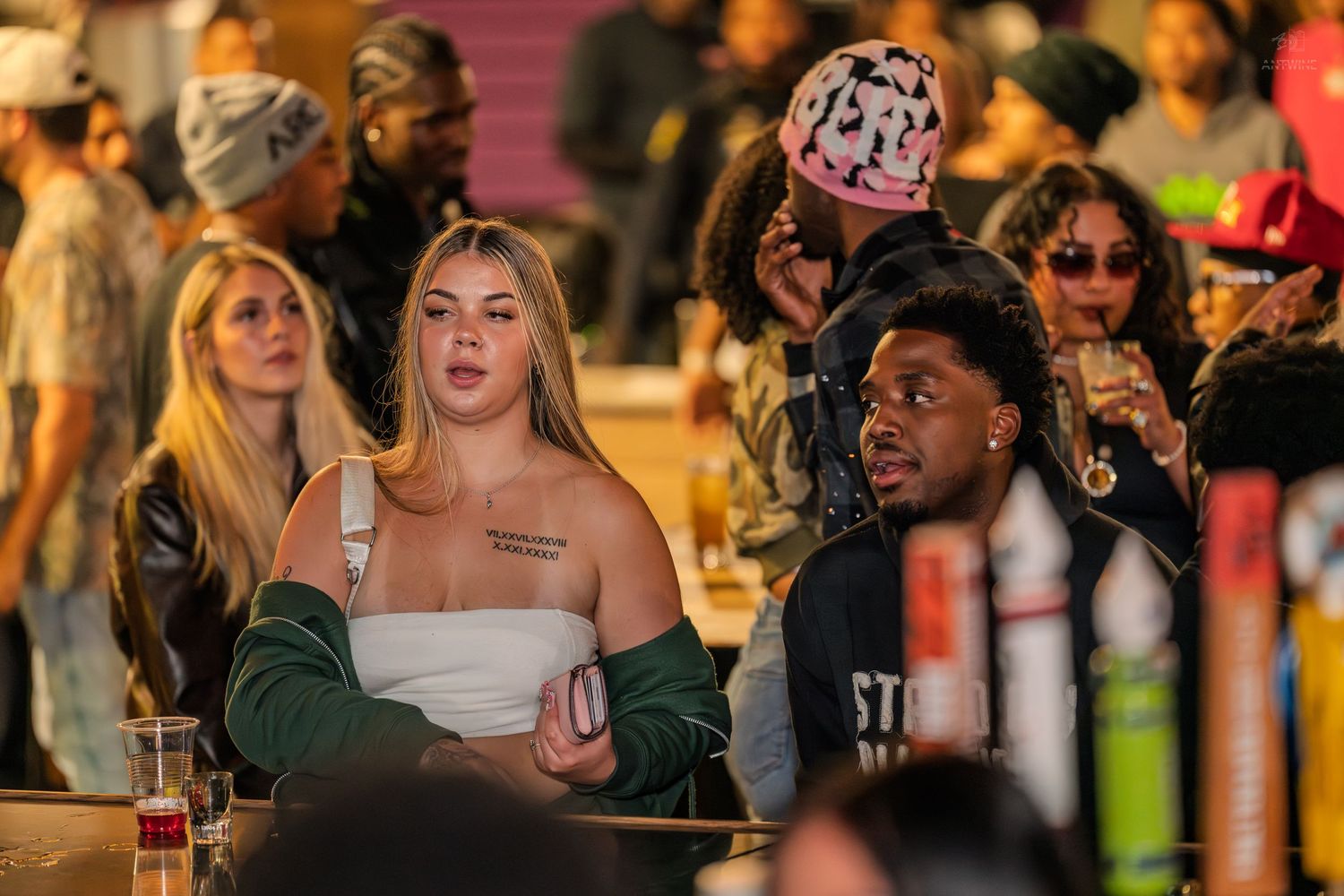 Diverse crowd of young adults socializing at a lively bar event with drinks in hand.