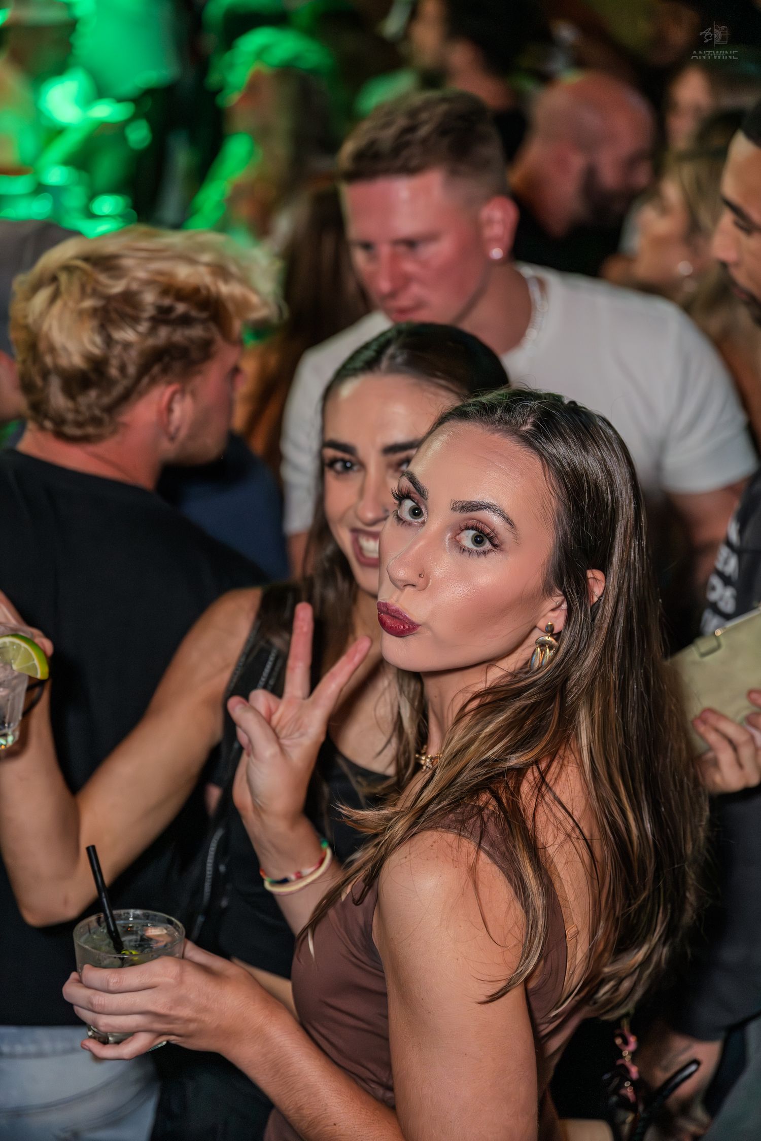Young woman making a peace sign and funny face at a packed nightclub party.