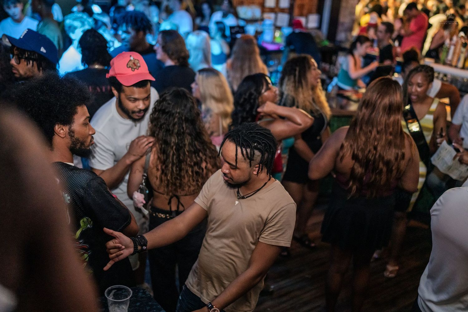 Young adults dancing at a lively nightclub party with blue and warm ambient lighting.