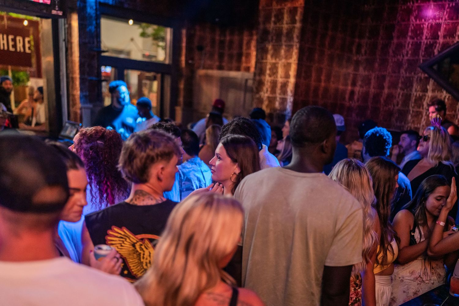 Diverse crowd of people mingling and socializing at a busy nightclub with colorful lighting.