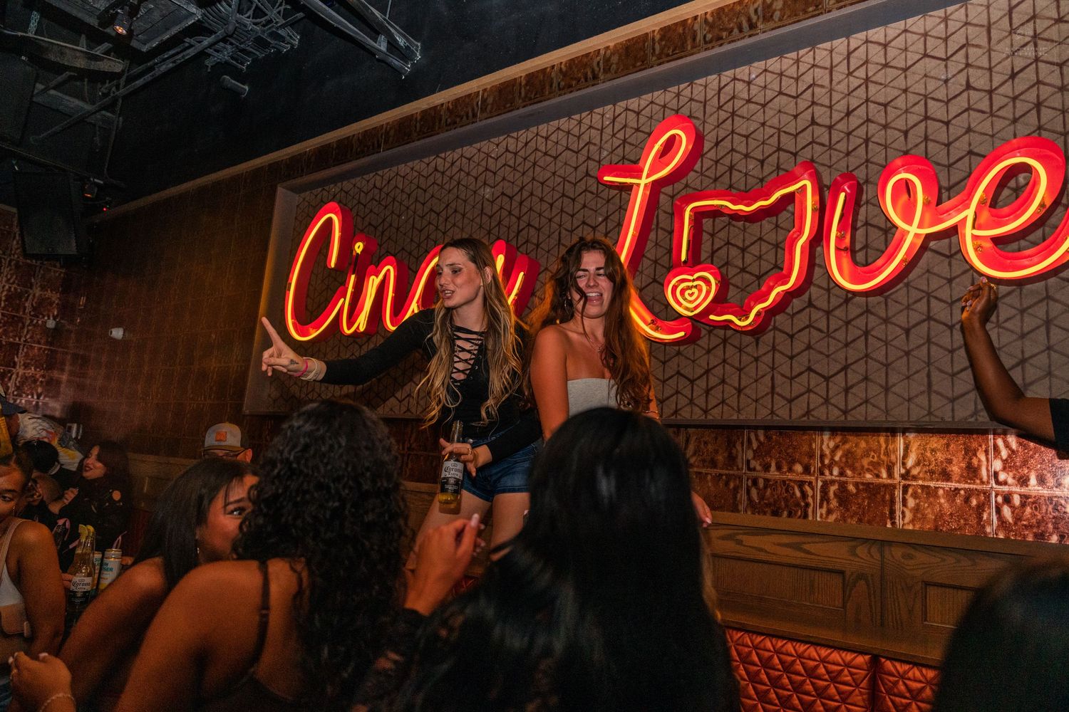Two women posing and celebrating under the Cincinnati Love neon sign at a bar.