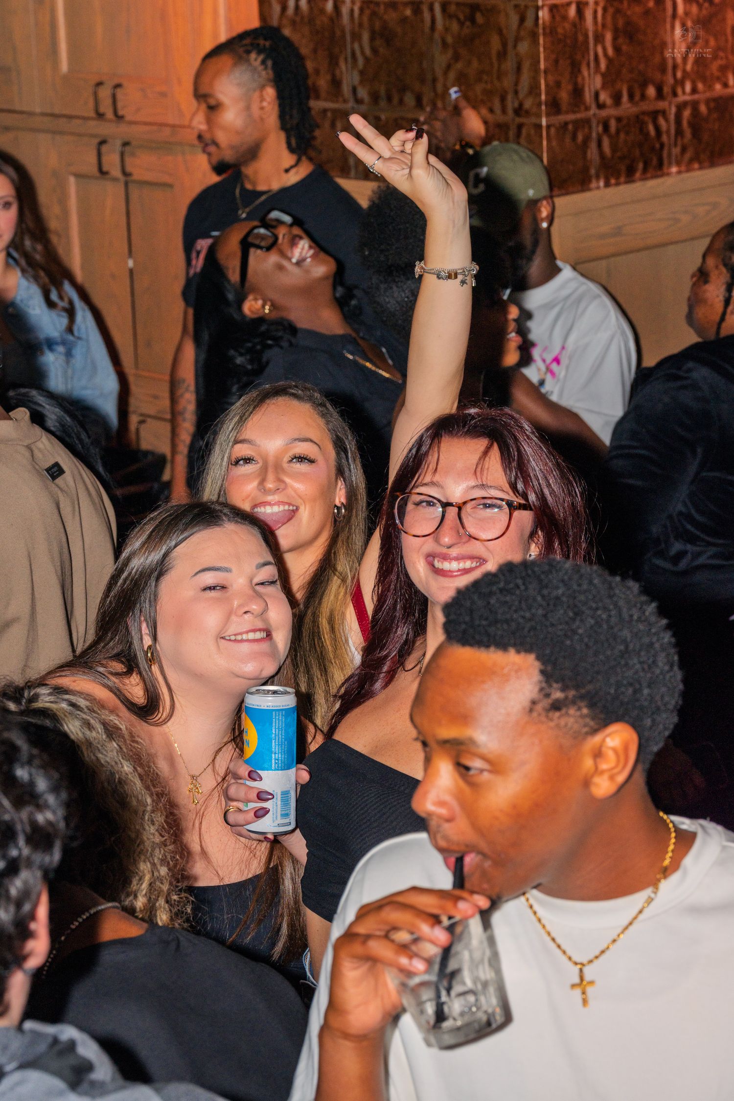 Group of smiling young women posing together at a lively indoor party with drinks.