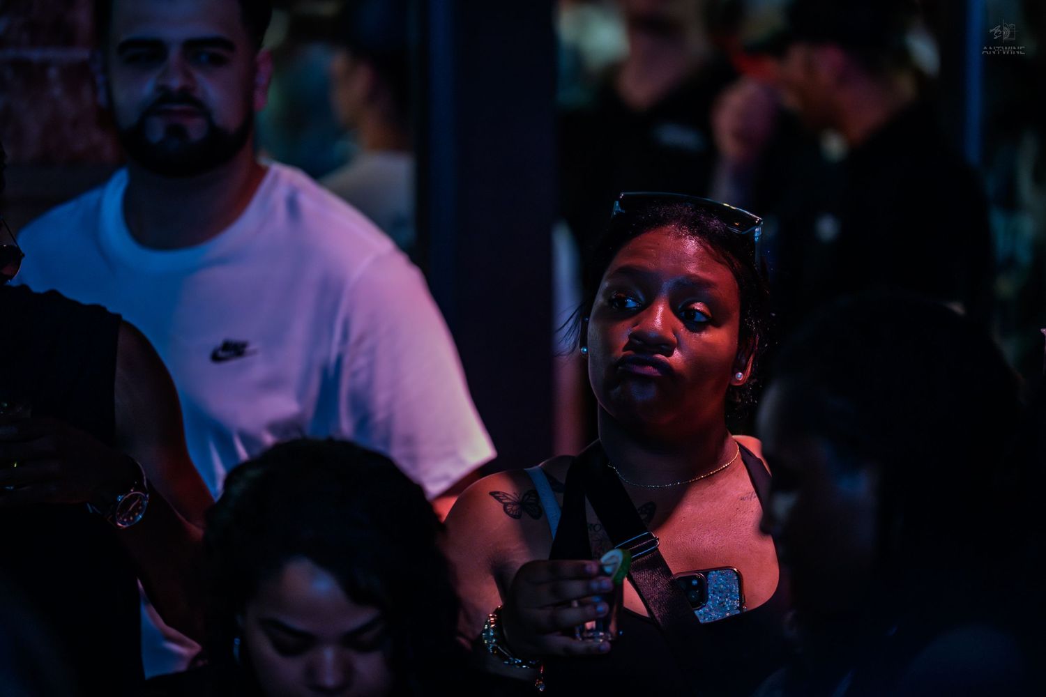 Woman with sunglasses on head looking up in dark moody nightclub setting.
