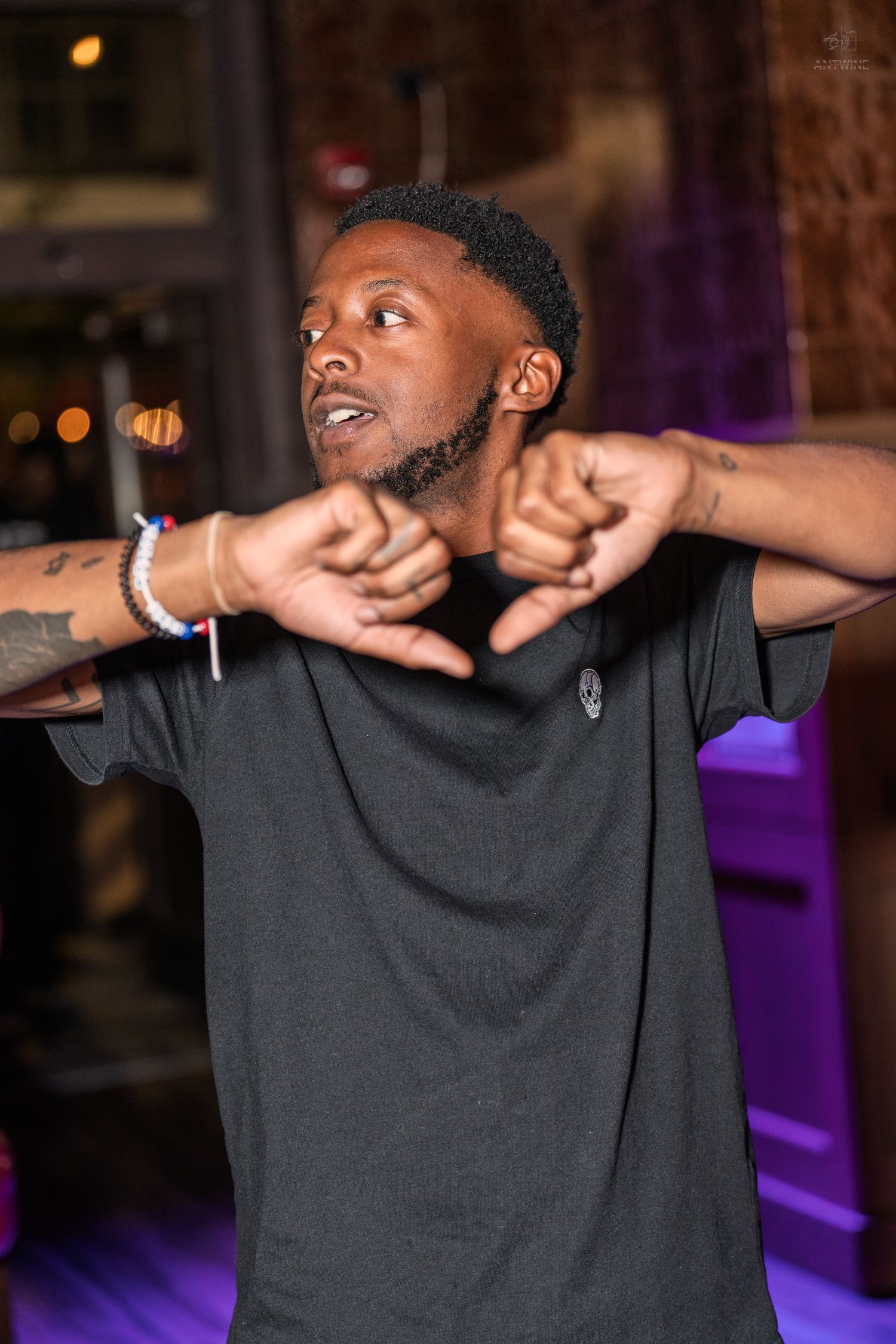 Man in black t-shirt striking a dynamic pose with arms crossed at a nightclub.