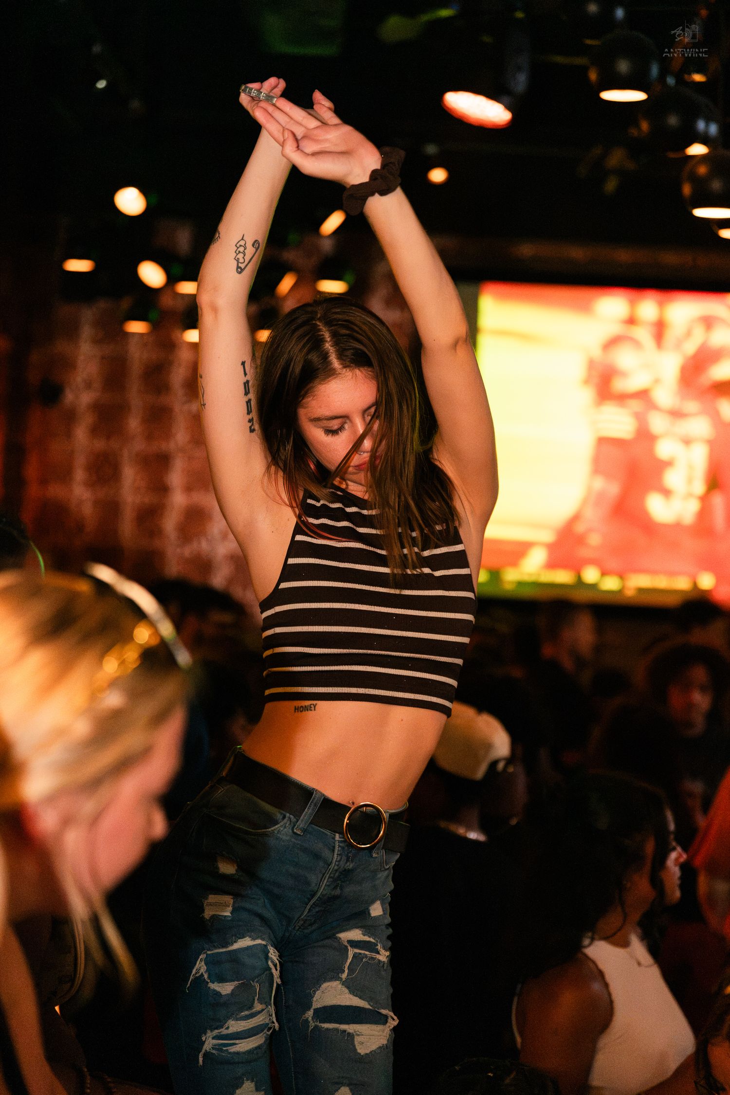 Young woman in striped crop top dancing with arms raised at a lively nightclub event.