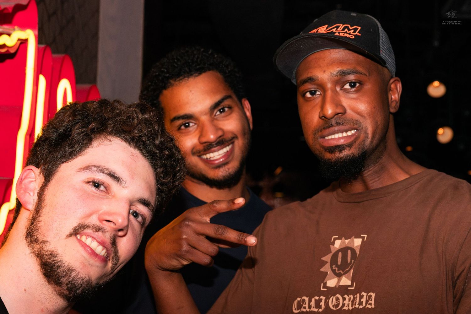 Three young men smiling and posing together at a nightclub event.