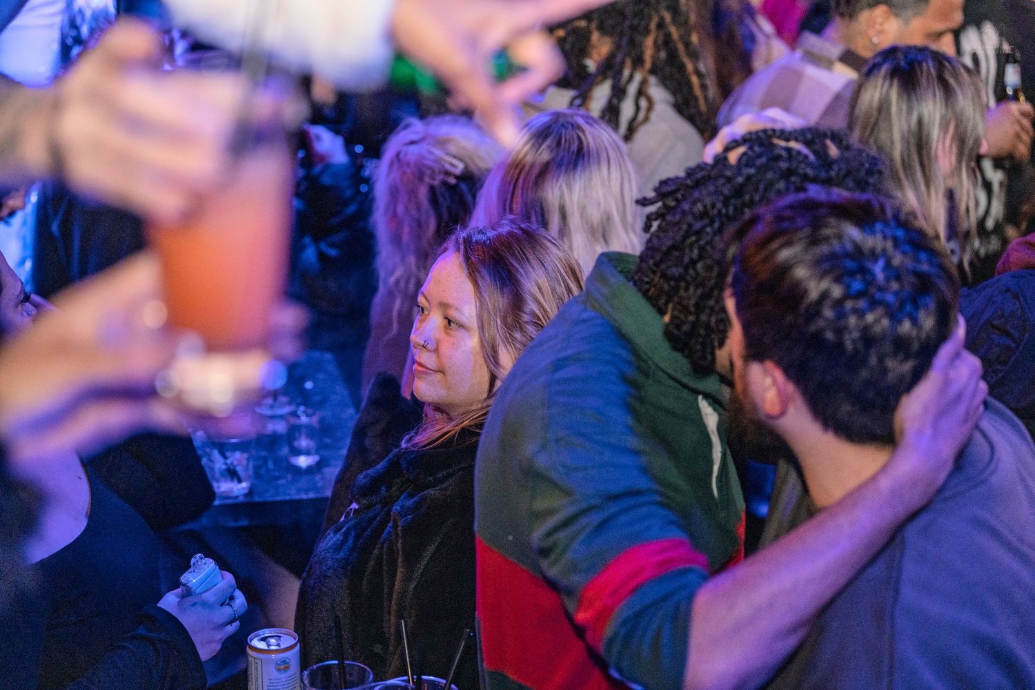 People socialize and relax with drinks under blue and purple lights at an indoor night event.