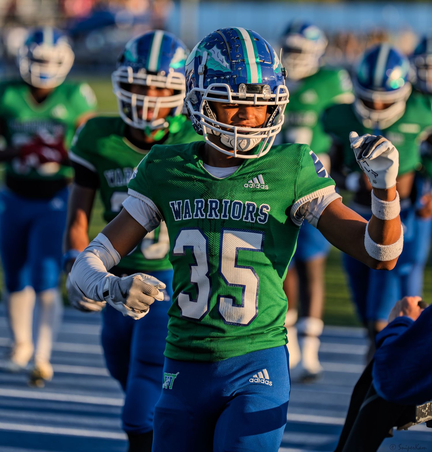 Warriors football player number 35 in green uniform runs onto field with teammates before a night game.