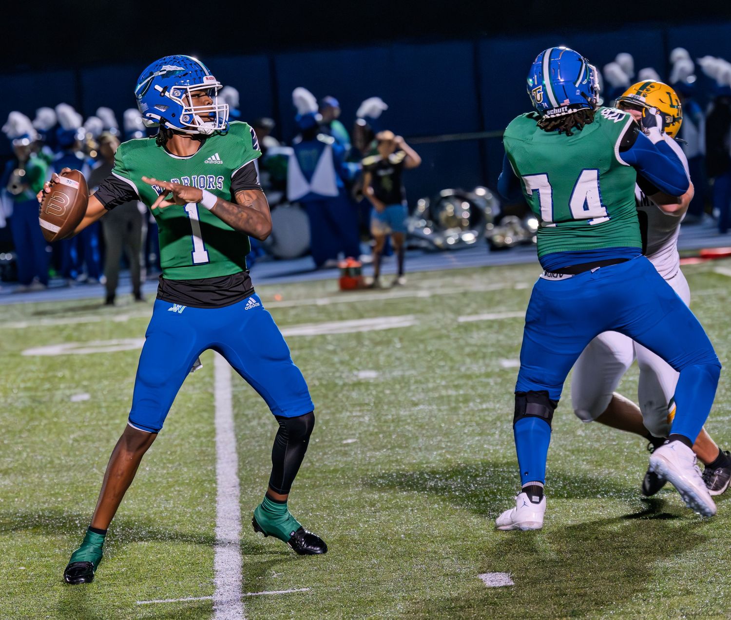 Warriors quarterback #7 in green and blue uniform prepares to throw a pass during a night game.