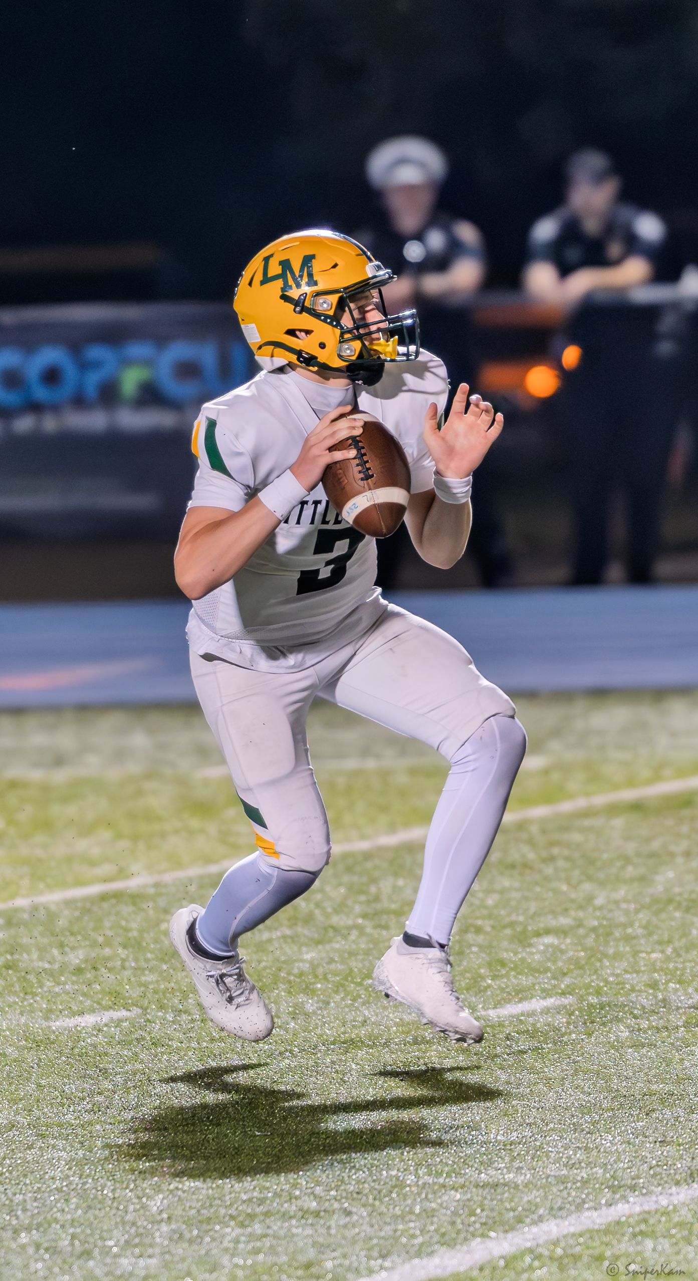 A quarterback in green and gold uniform drops back to pass during a high school football game.