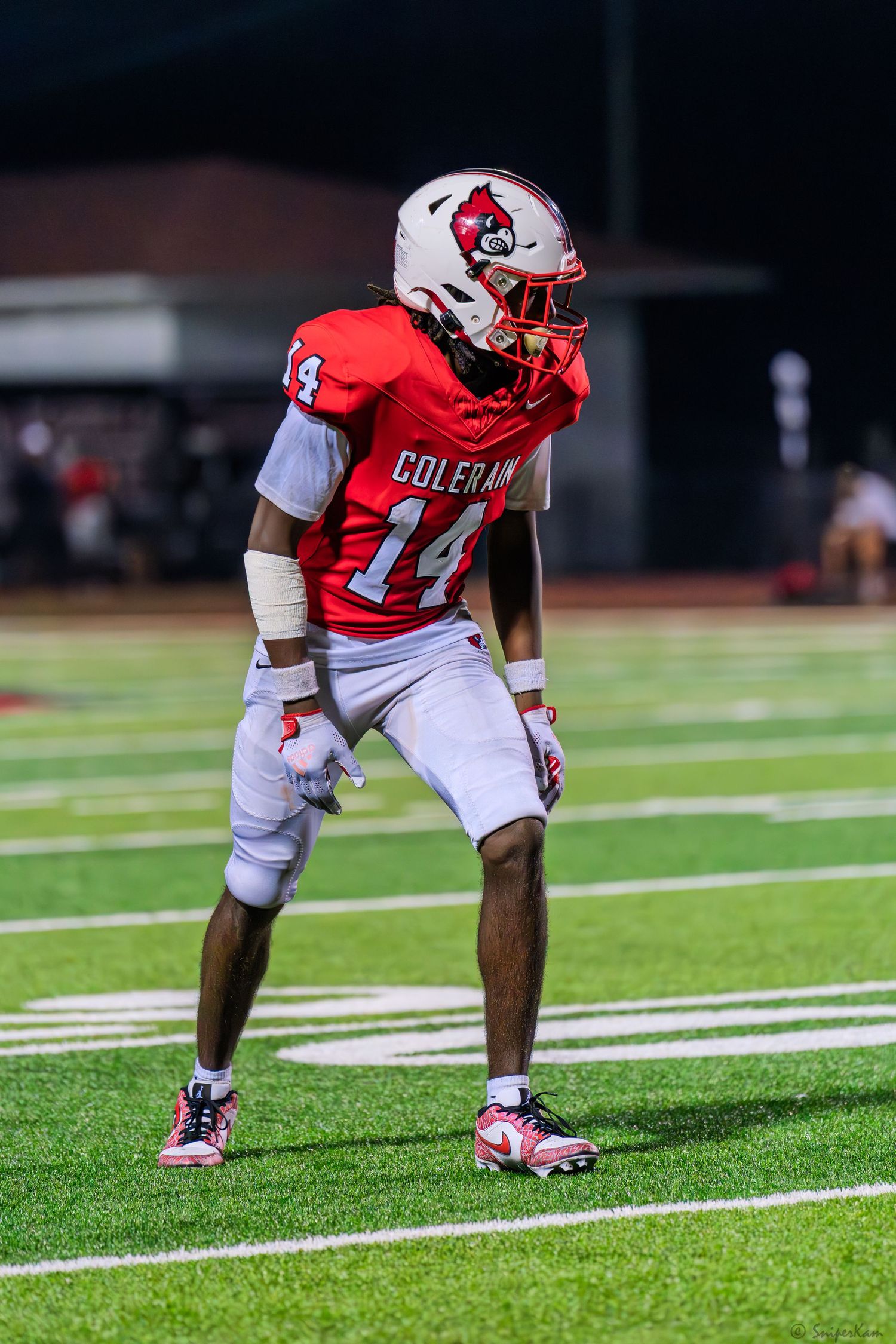 Colerain Cardinals football player number 14 in red uniform stands ready on turf field.