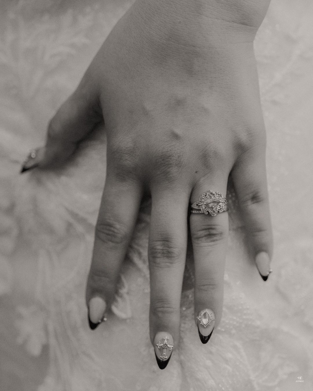 Close-up black and white photo of a bride's hand showcasing a diamond engagement ring and elegant black-tipped nails.