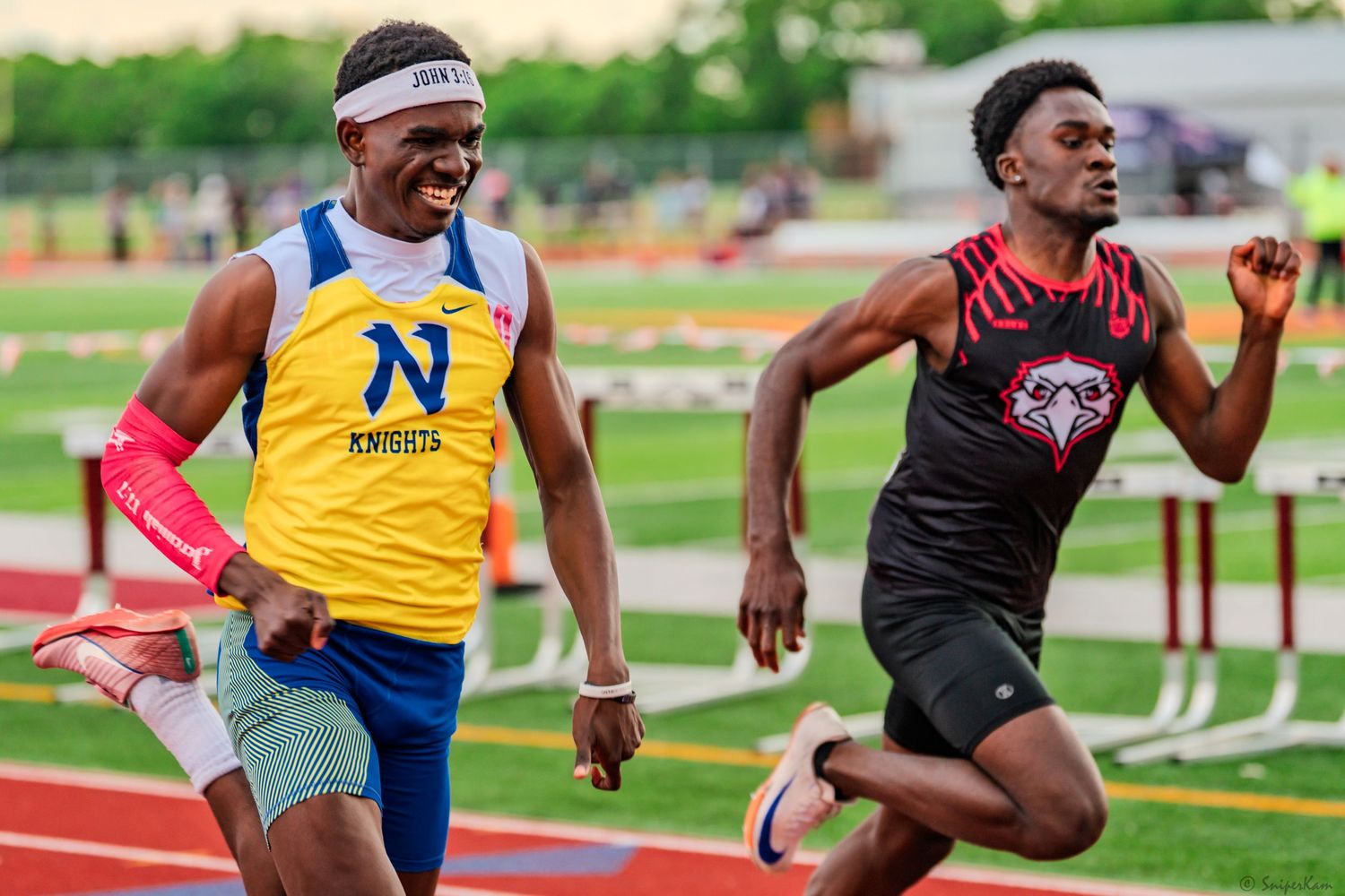 Two male sprinters compete intensely on a red track, one wearing a blue Knights jersey and headband.
