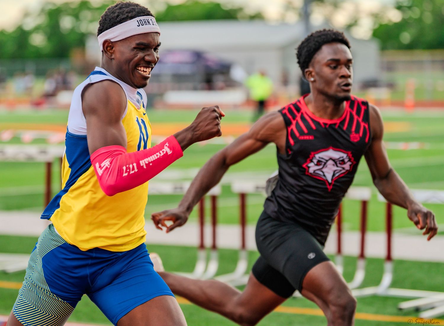 Two male sprinters race neck and neck on a track, one in a blue Knights jersey celebrating.