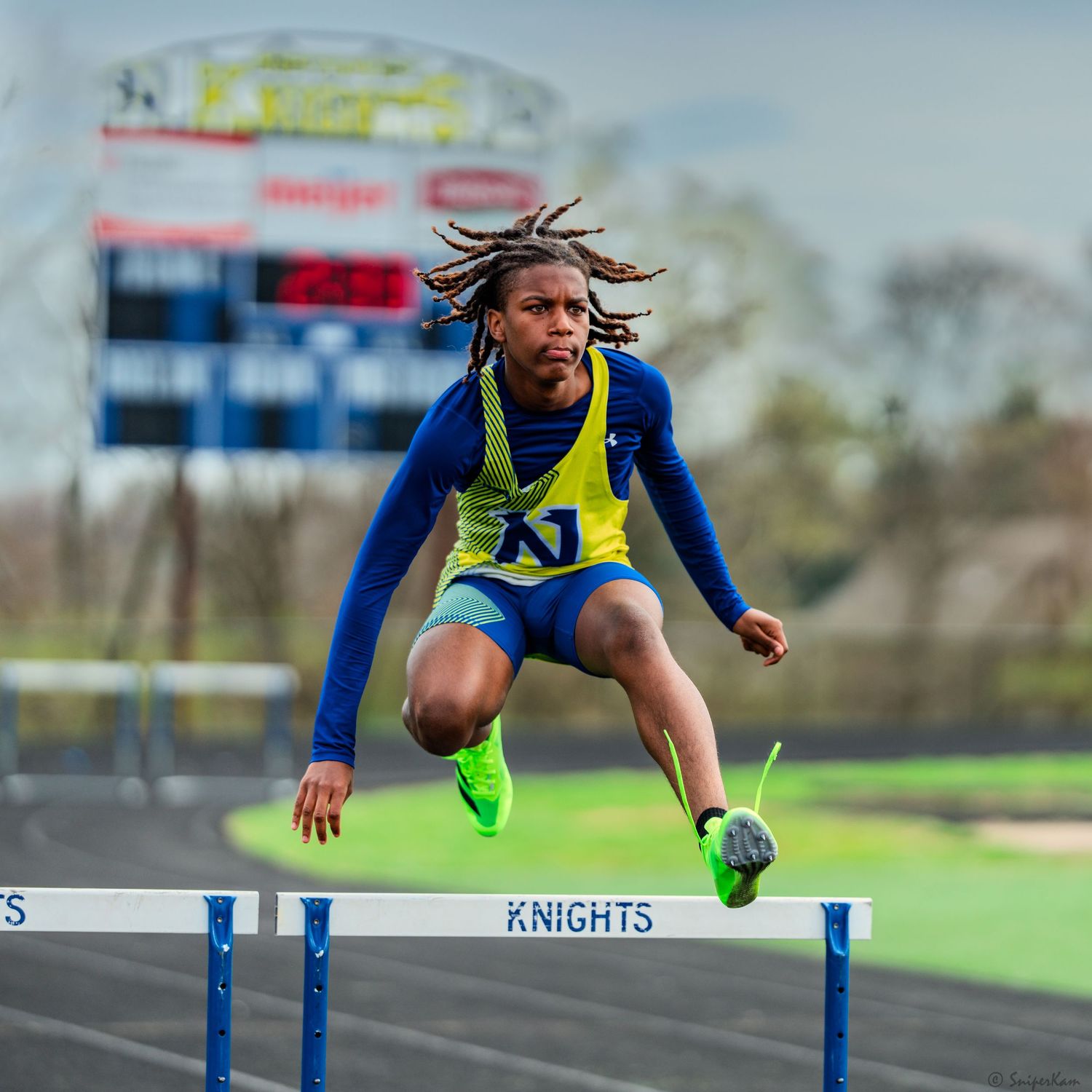 Young male athlete jumping over a hurdle on a Knights track field during competition.