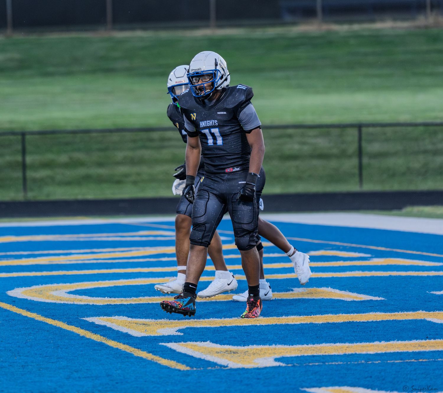 Two Knights football players in black uniforms celebrate in the blue end zone after scoring a touchdown.