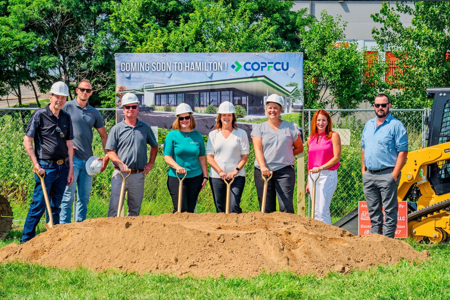 Group of seven people in hard hats holding shovels at COPFCU groundbreaking ceremony outdoors.