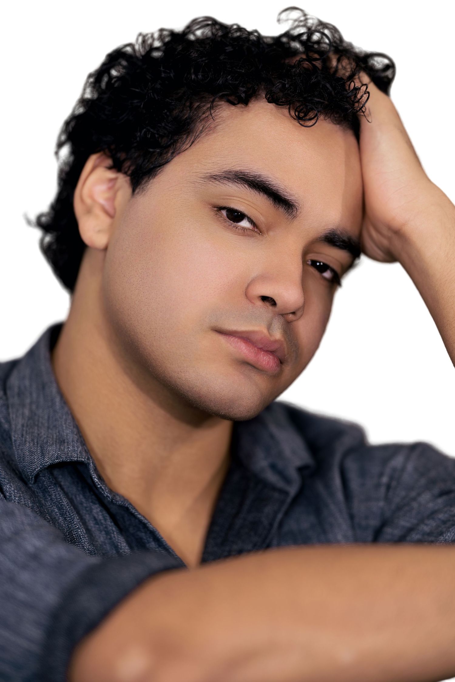 Young man with curly hair resting hand on head in a relaxed studio portrait pose.