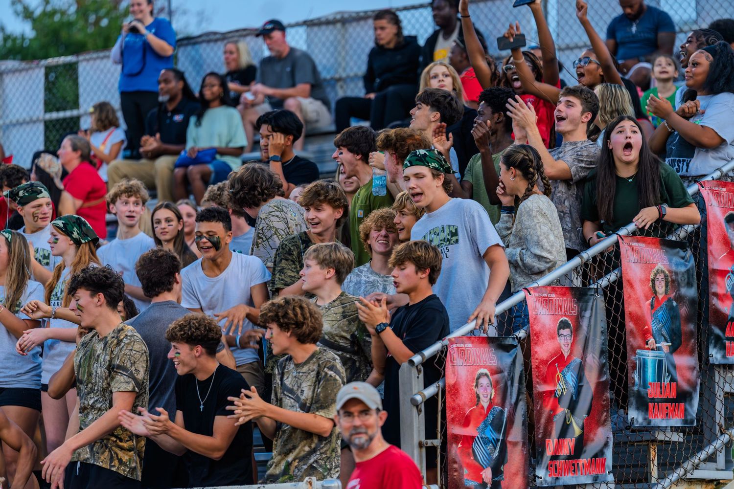 Energetic high school football fans cheer enthusiastically from the stands during an exciting Friday night football game.