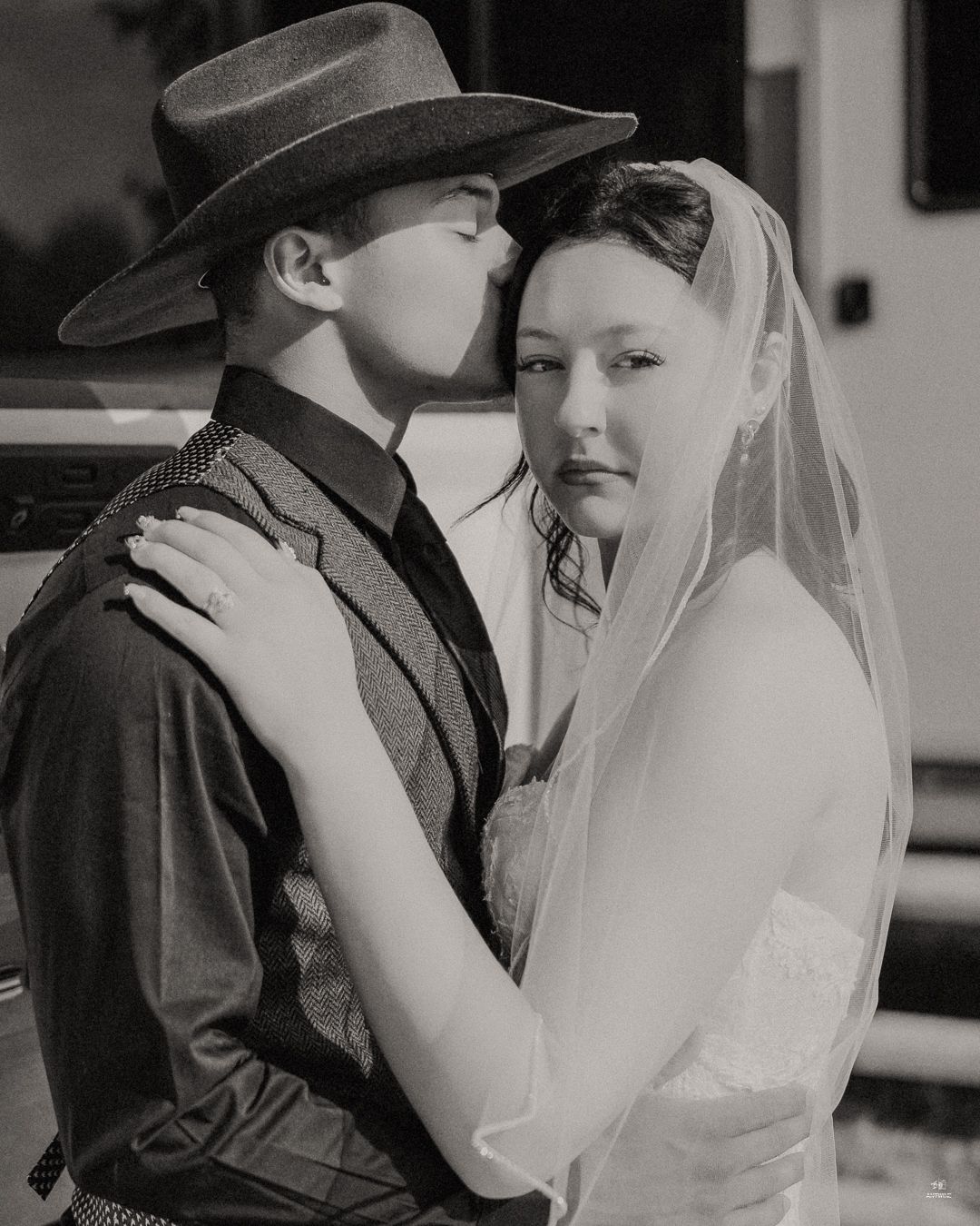 Black and white photo of groom in cowboy hat kissing bride in veil at wedding.